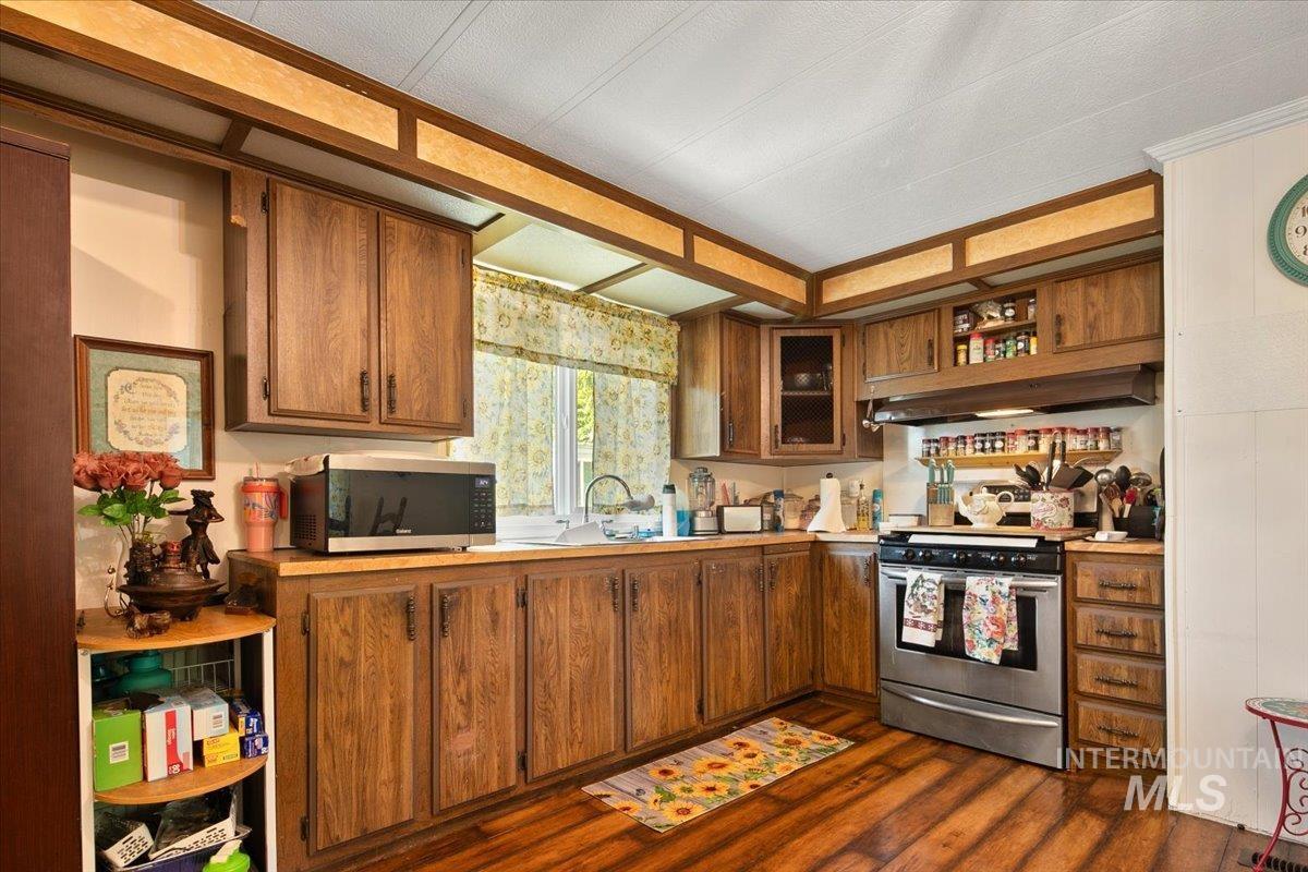 Kitchen with light countertops, brown cabinetry, appliances with stainless steel finishes, dark wood finished floors, and open shelves