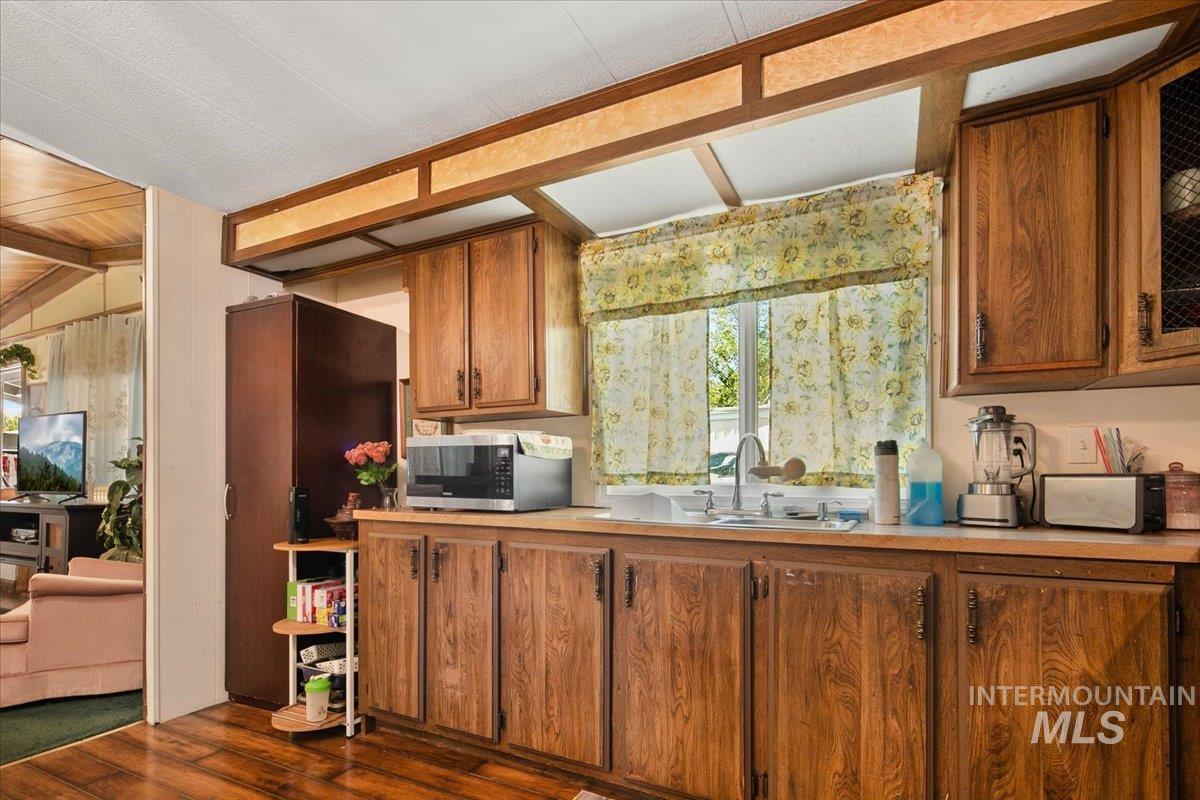 Kitchen with brown cabinets, light countertops, dark wood finished floors, stainless steel microwave, and wooden walls