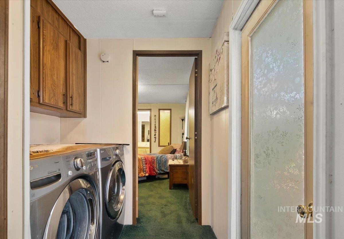 Washroom featuring dark colored carpet, a textured ceiling, cabinet space, and washer and clothes dryer