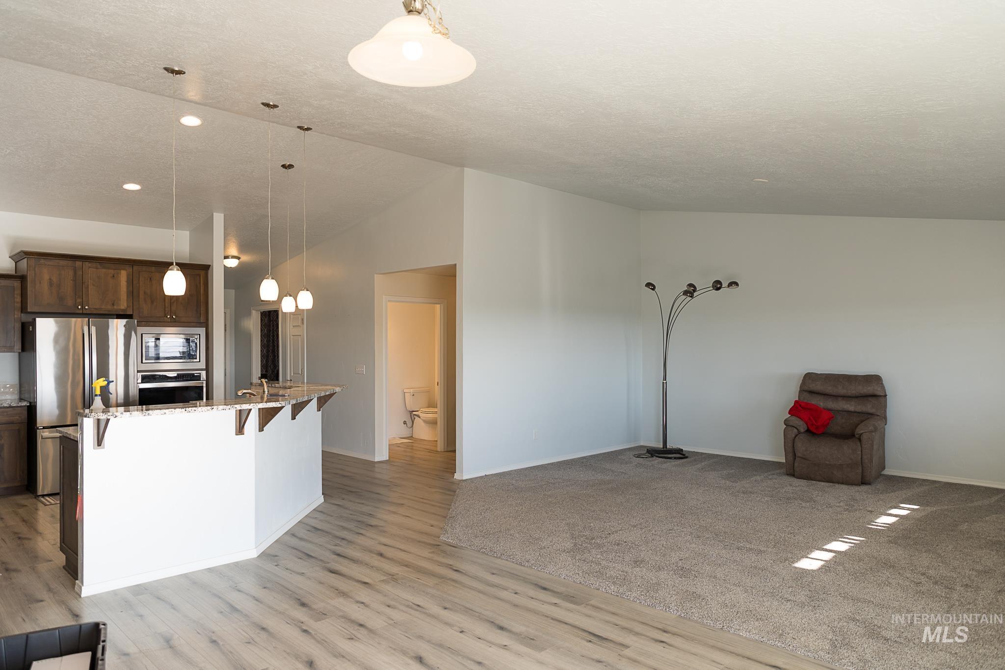 Kitchen with a kitchen bar, light stone countertops, hanging light fixtures, appliances with stainless steel finishes, and open floor plan