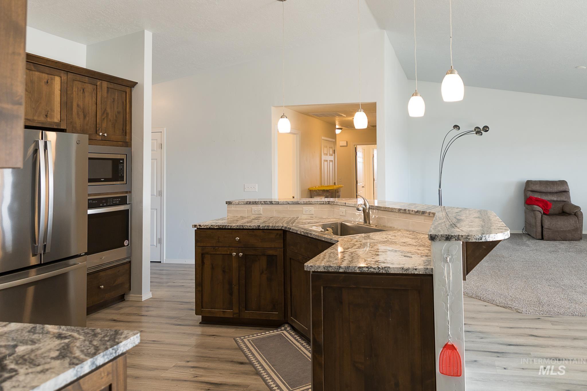 Kitchen with appliances with stainless steel finishes, dark brown cabinets, pendant lighting, open floor plan, and light stone counters