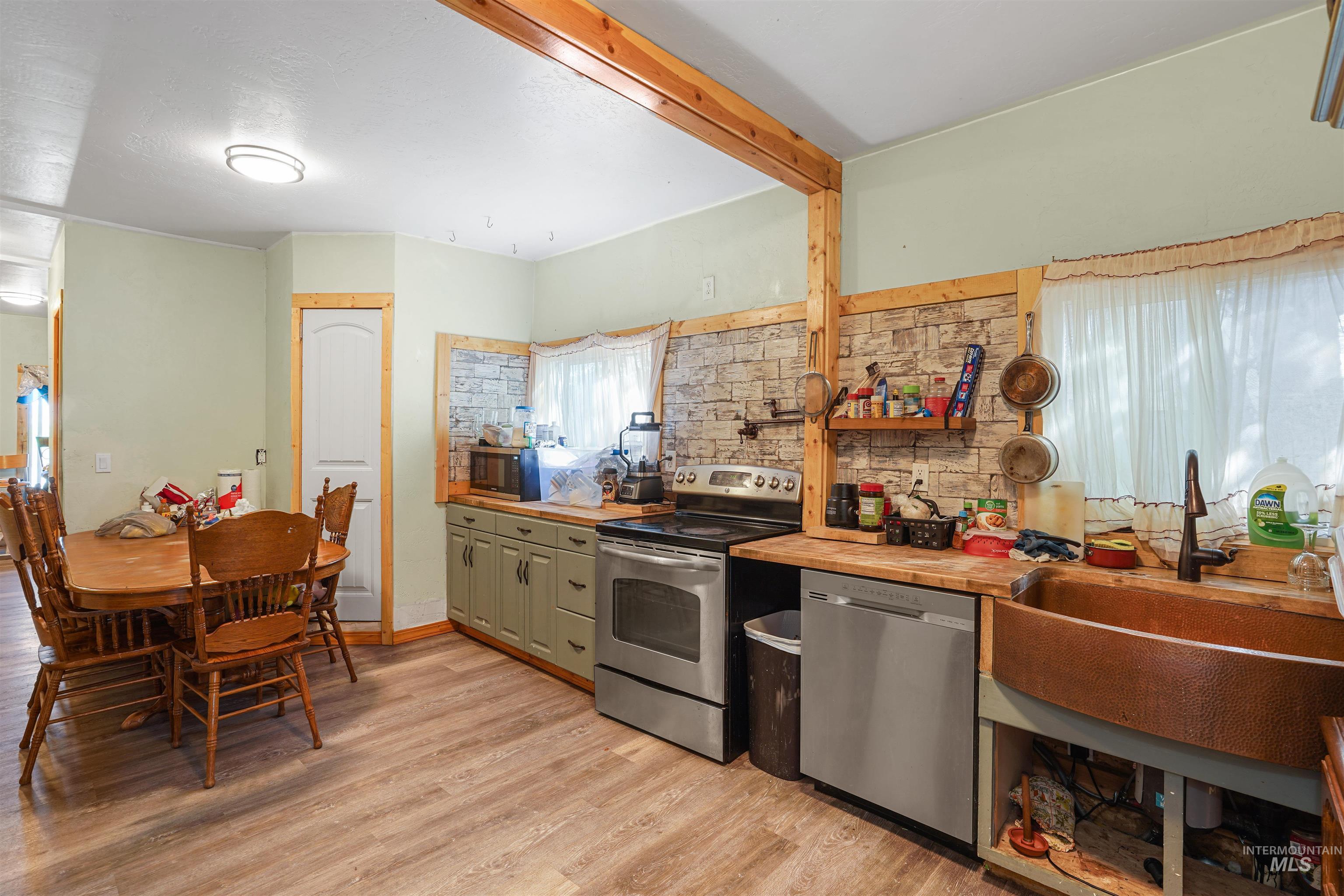 Kitchen with appliances with stainless steel finishes, light wood-type flooring, beamed ceiling, and wood counters