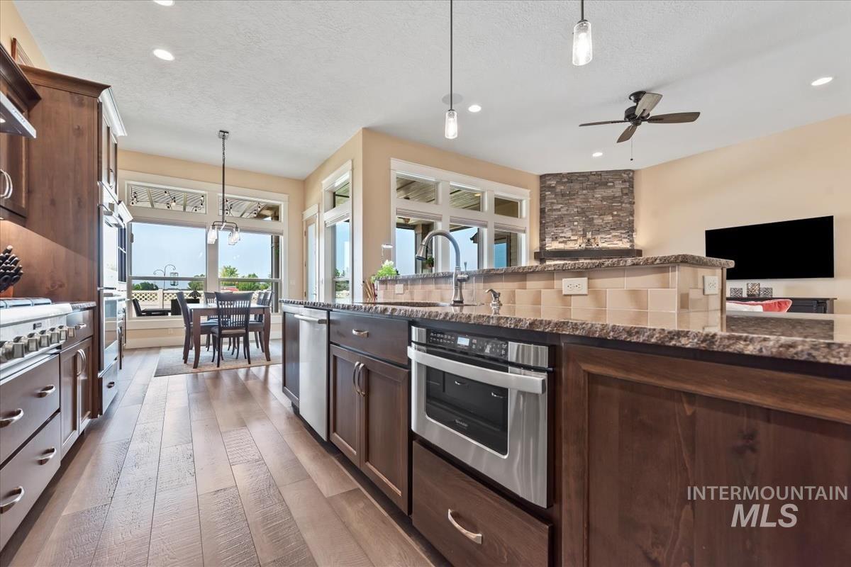 Kitchen with decorative light fixtures, dark brown cabinetry, dark stone counters, light wood finished floors, and recessed lighting