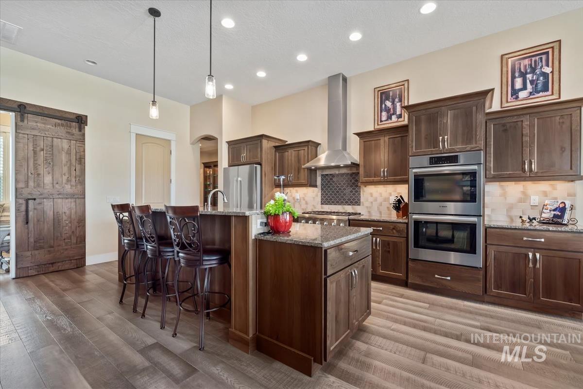 Kitchen with a barn door, light stone counters, a breakfast bar area, a center island with sink, and stainless steel appliances
