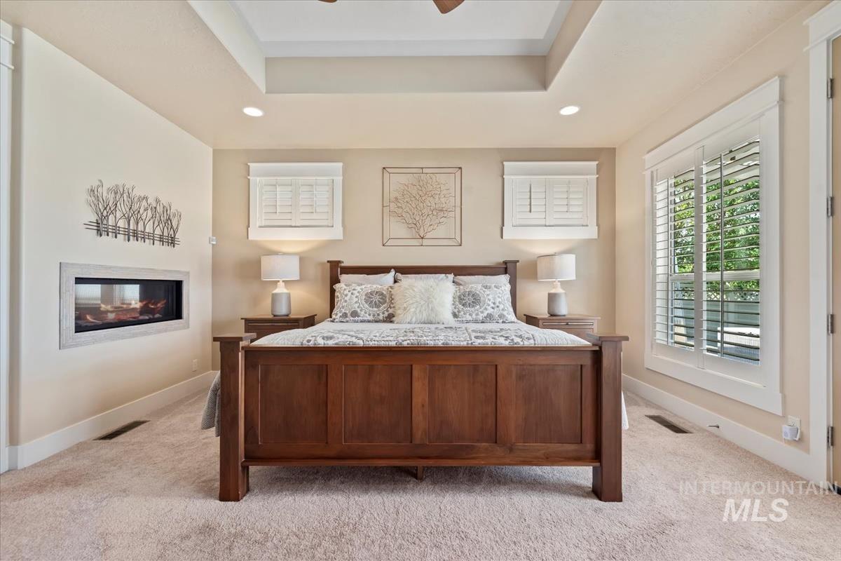 Bedroom with a raised ceiling, carpet floors, recessed lighting, and a glass covered fireplace