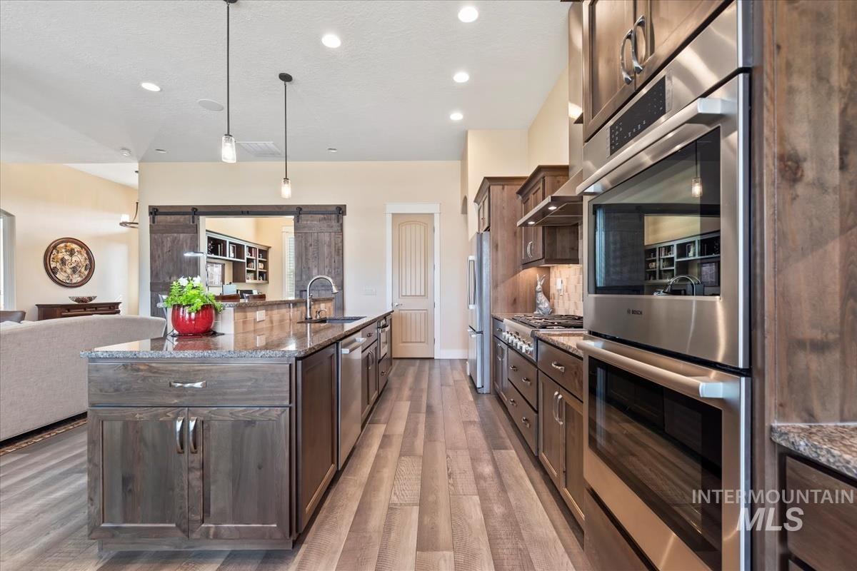 Kitchen with a barn door, stainless steel appliances, dark stone countertops, pendant lighting, and dark brown cabinetry
