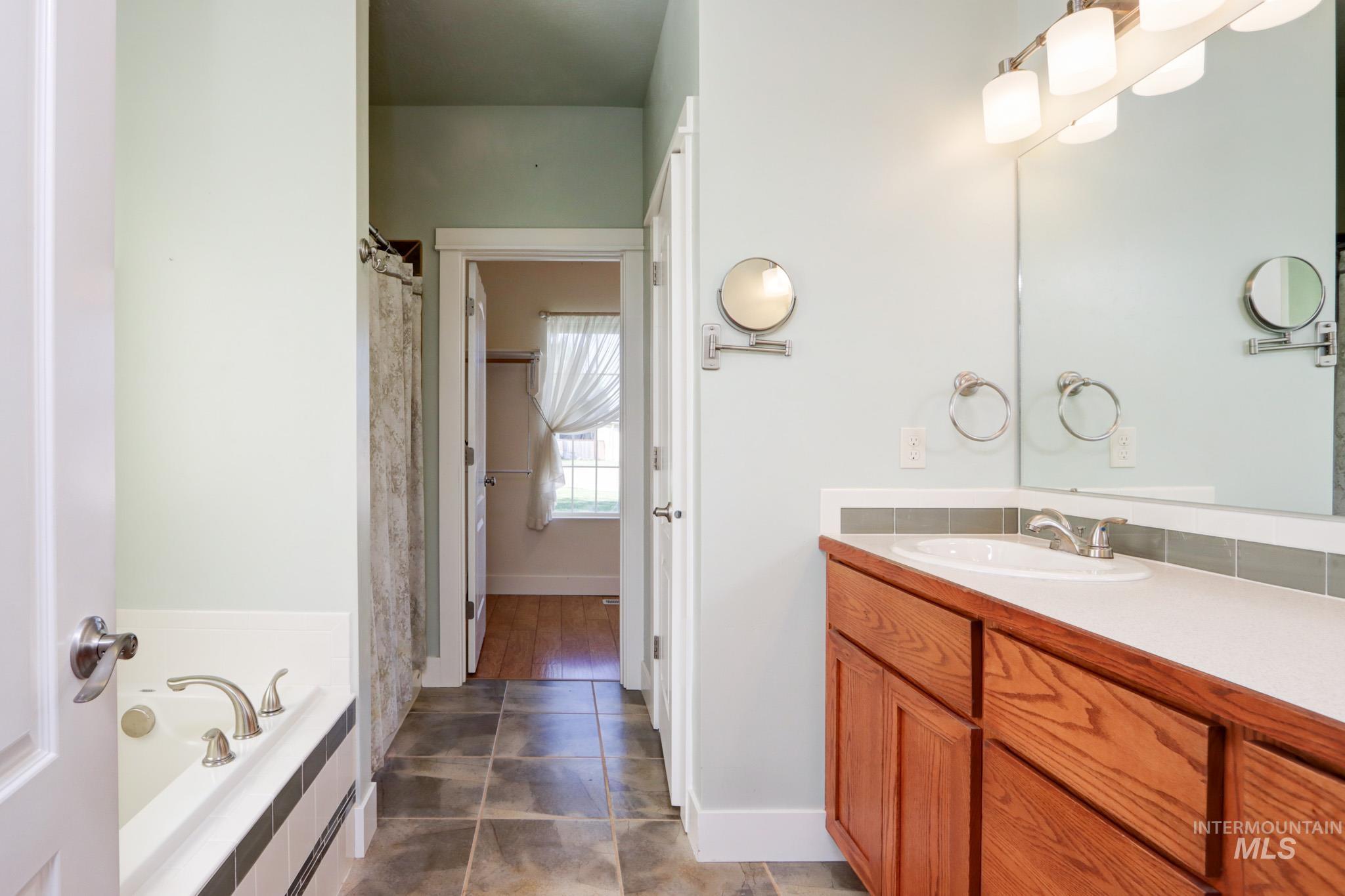 Full bathroom featuring vanity, a garden tub, and dark tile patterned floors