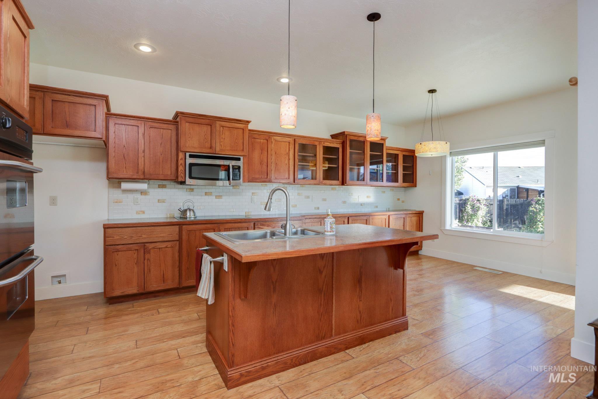 Kitchen featuring brown cabinetry, tasteful backsplash, glass insert cabinets, a breakfast bar area, and recessed lighting