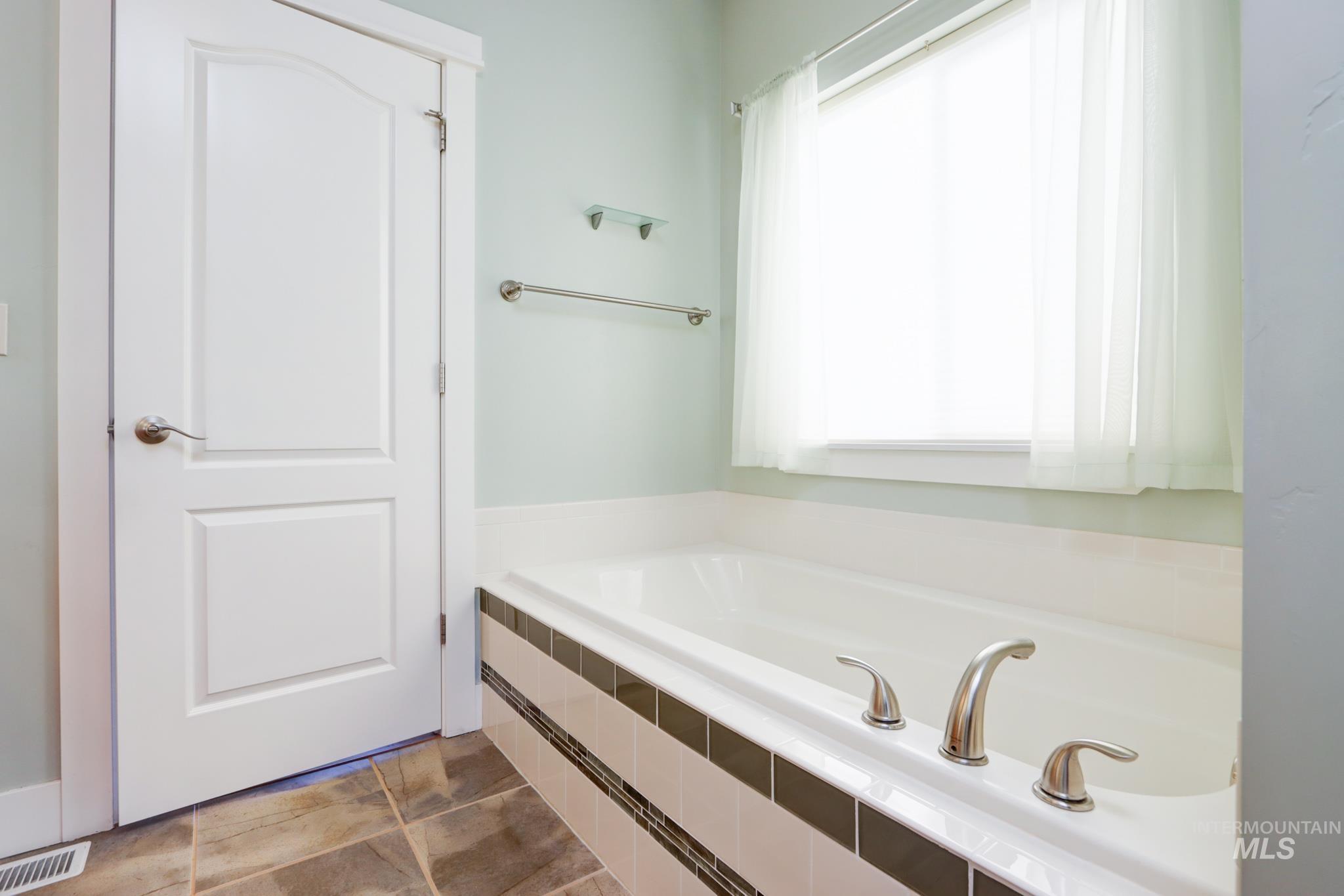 Full bath featuring healthy amount of natural light, a bath, and dark tile patterned floors