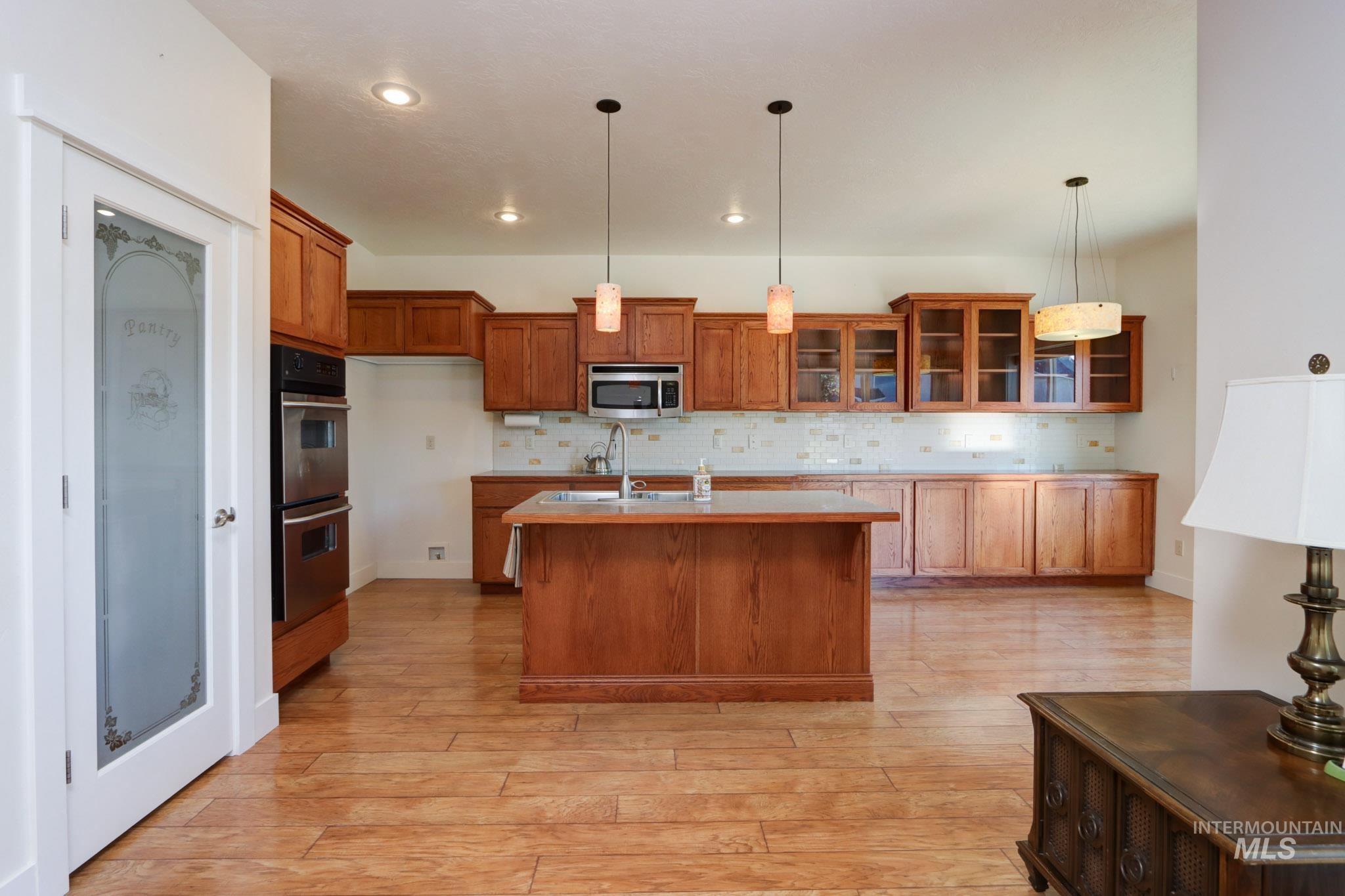 Kitchen with backsplash, brown cabinets, glass insert cabinets, recessed lighting, and light countertops