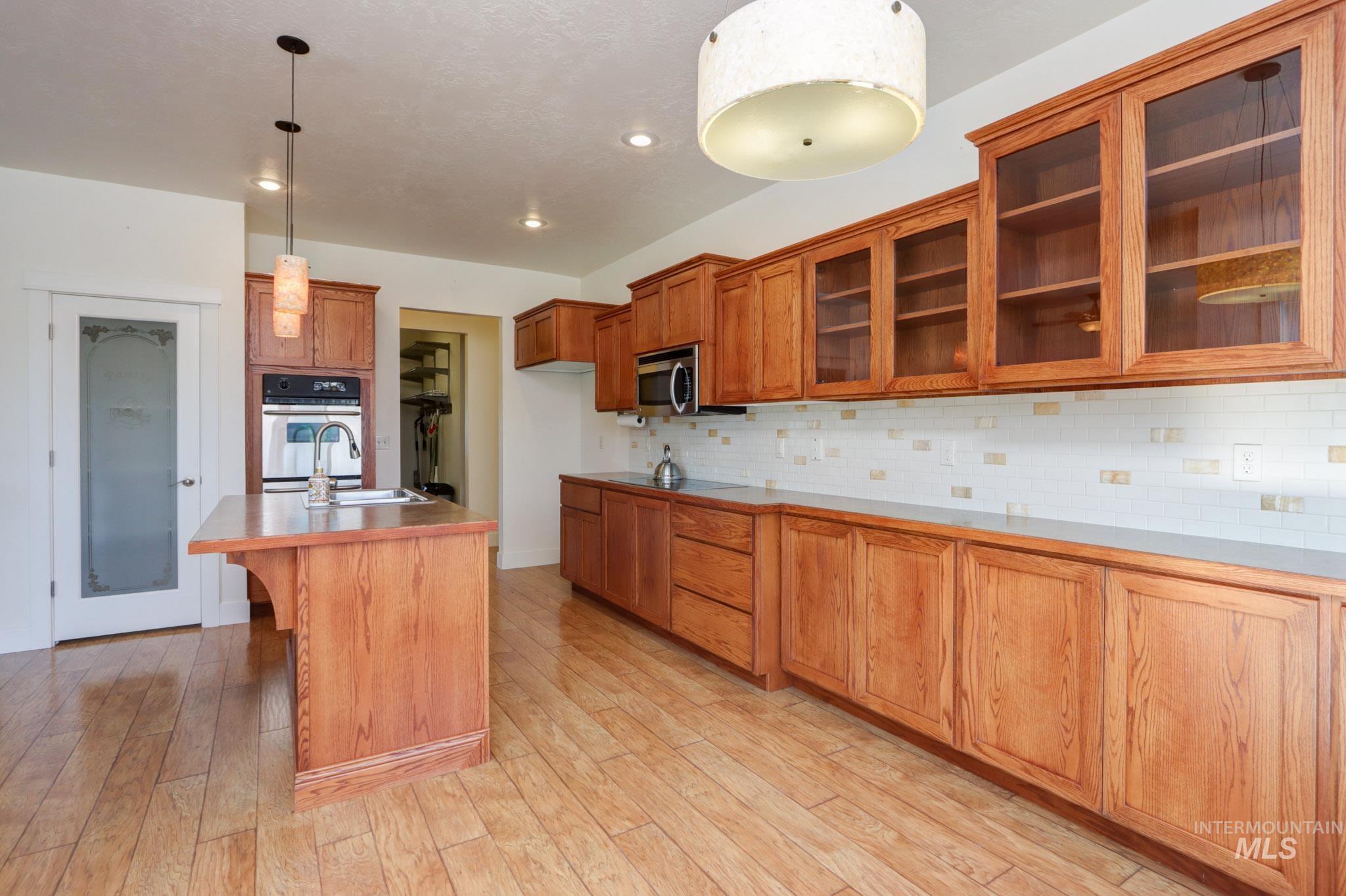 Kitchen featuring brown cabinets, a kitchen breakfast bar, glass insert cabinets, hanging light fixtures, and a center island with sink