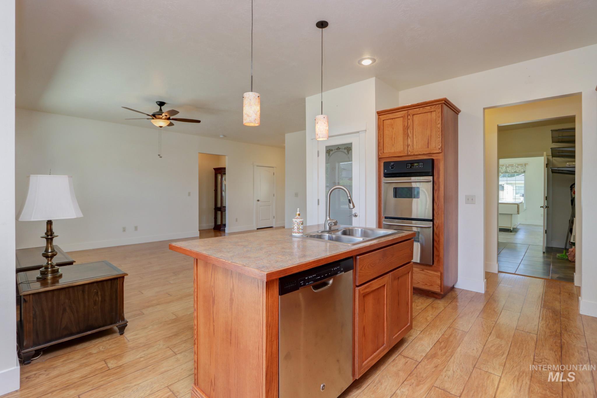 Kitchen with hanging light fixtures, a center island with sink, stainless steel appliances, light wood-type flooring, and recessed lighting
