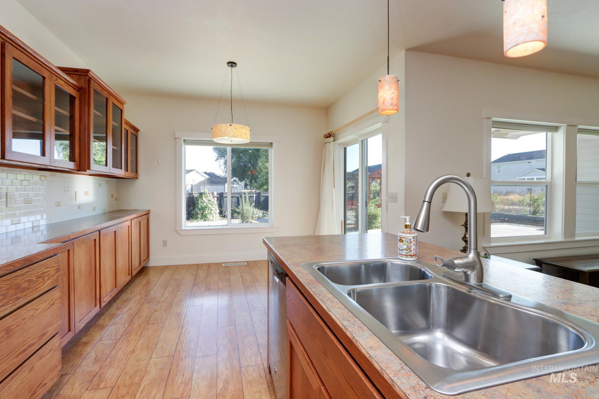 Kitchen with brown cabinetry, pendant lighting, glass insert cabinets, and plenty of natural light