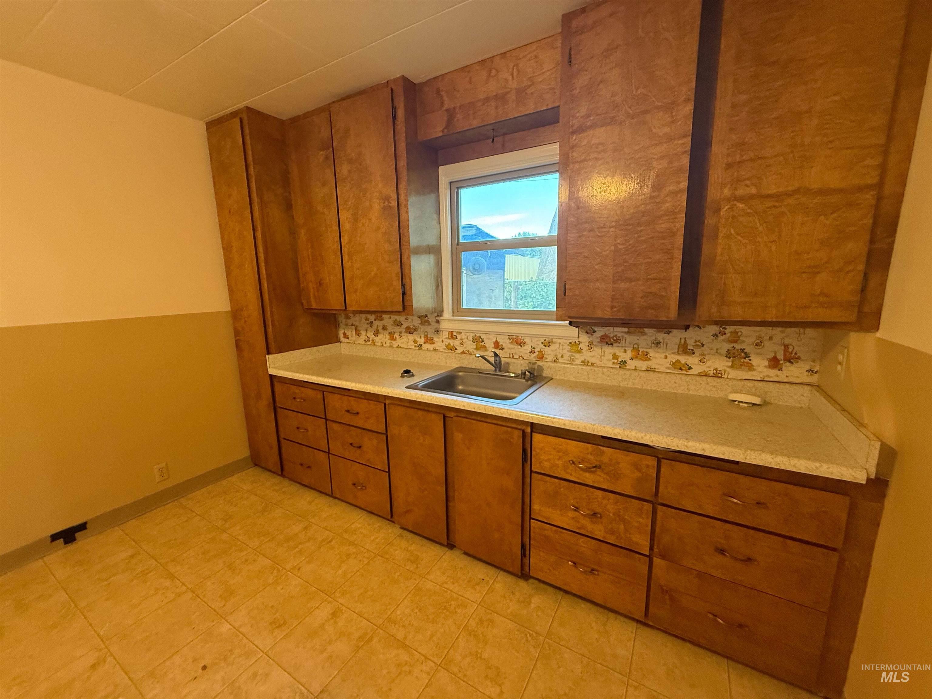 Kitchen with brown cabinetry, light countertops, and tasteful backsplash