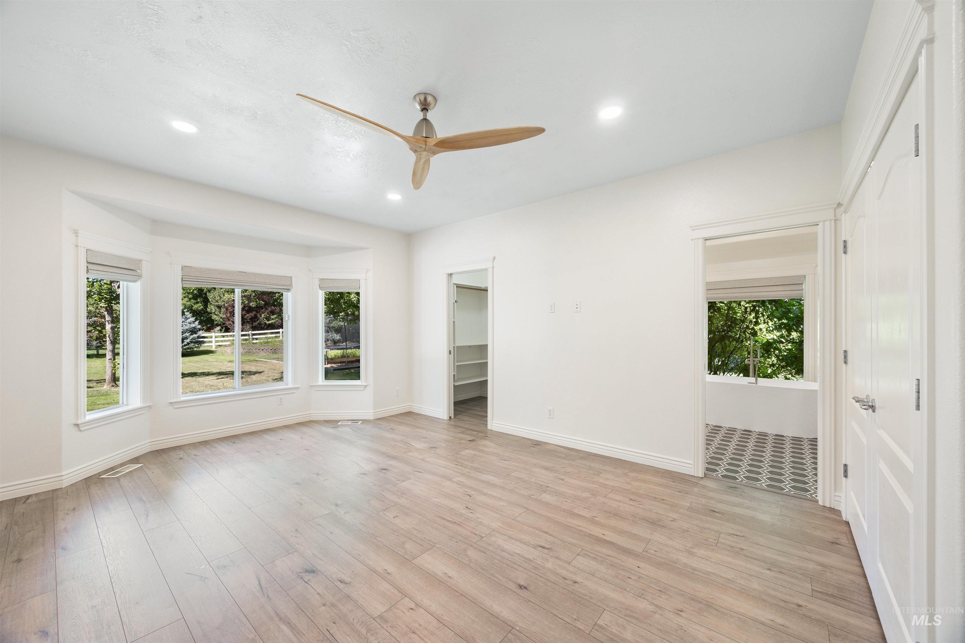 Unfurnished bedroom featuring a spacious closet, multiple windows, ceiling fan, light wood-style flooring, and recessed lighting