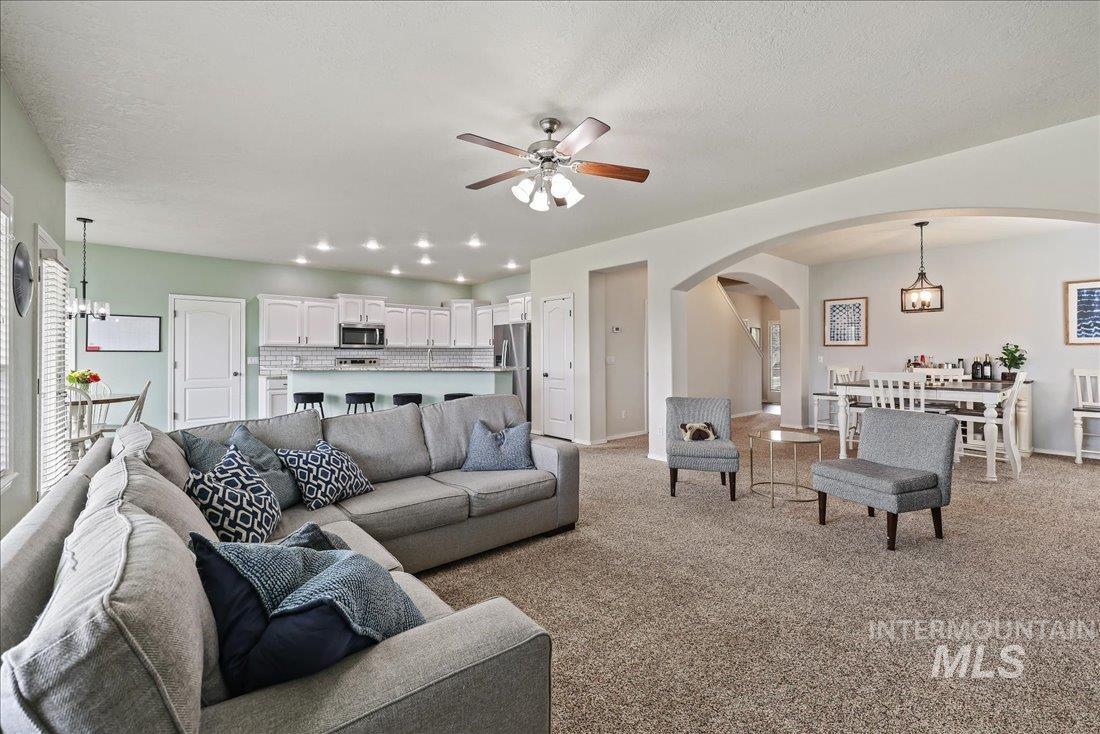 Carpeted living room with a chandelier, arched walkways, a ceiling fan, and recessed lighting