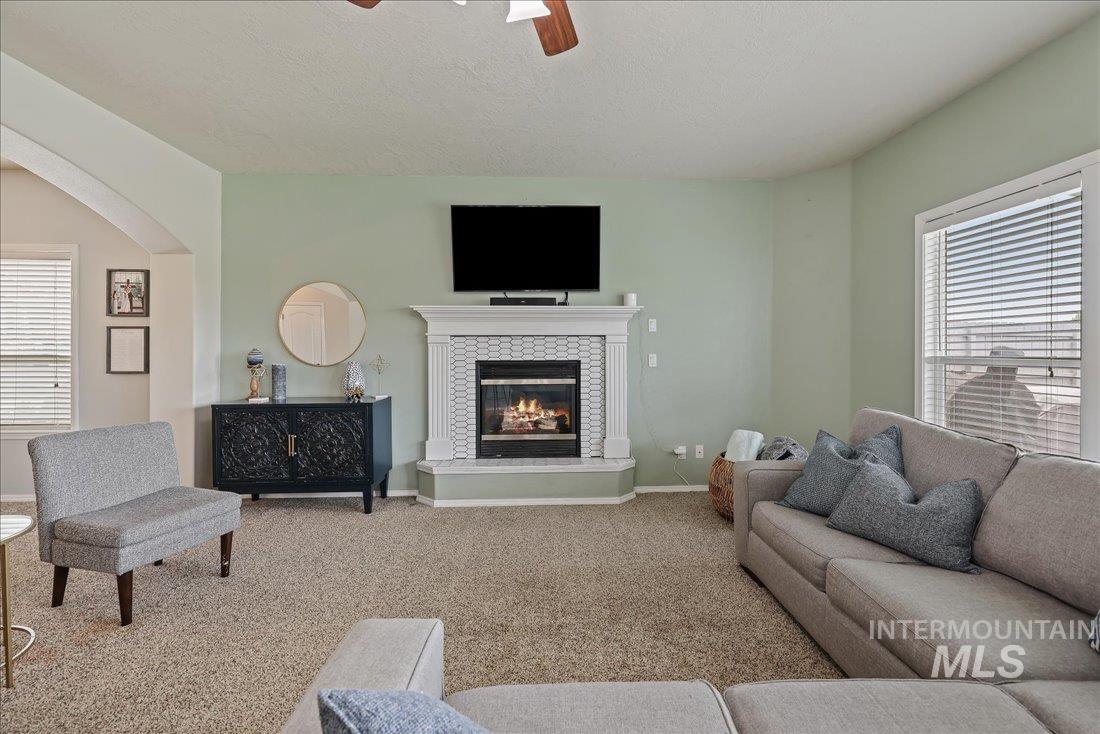 Living area featuring carpet floors, ceiling fan, a tile fireplace, arched walkways, and a textured ceiling
