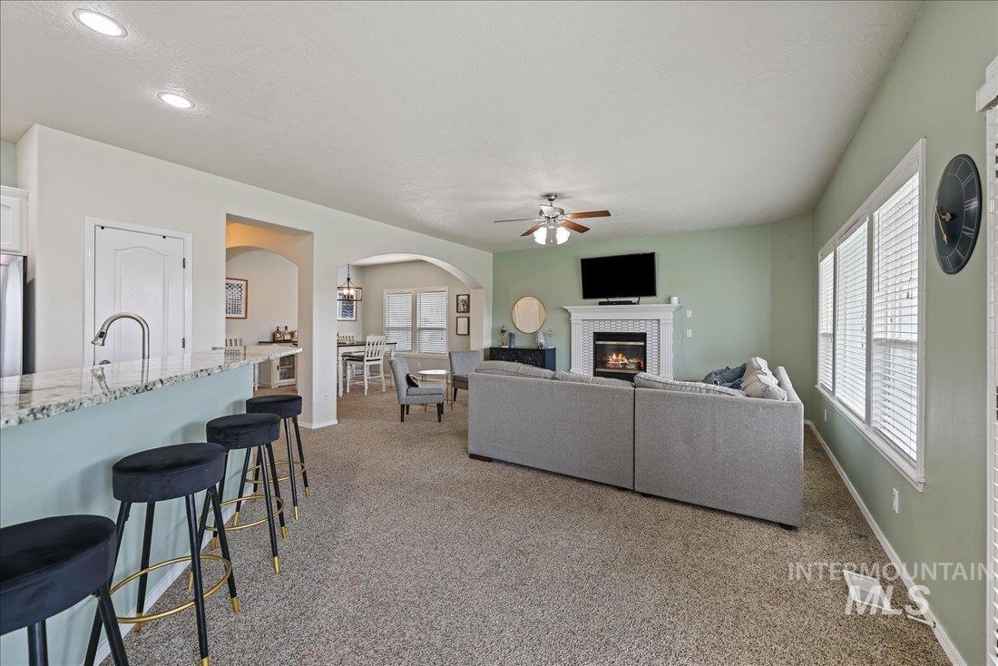 Living room with light carpet, a tile fireplace, a ceiling fan, arched walkways, and a textured ceiling