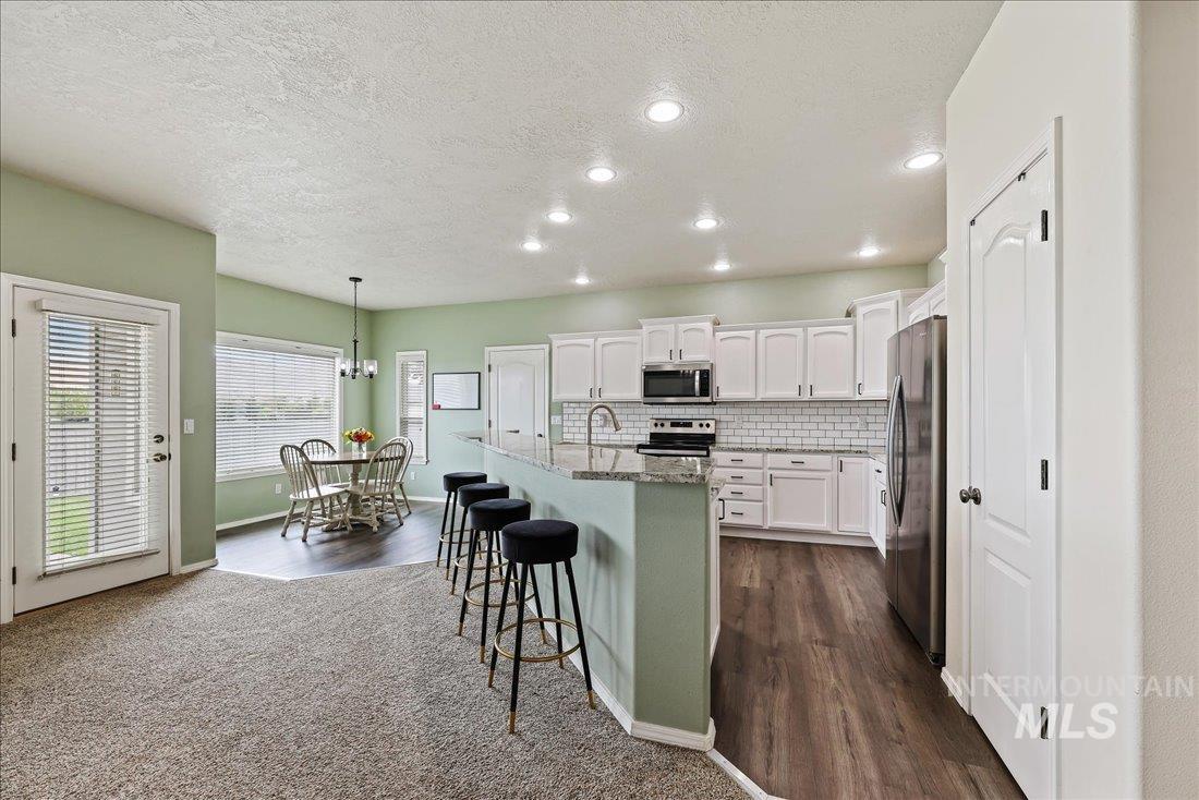 Kitchen featuring white cabinets, decorative backsplash, a kitchen breakfast bar, appliances with stainless steel finishes, and decorative light fixtures