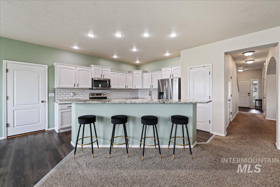 Kitchen featuring white cabinets, light stone counters, a breakfast bar, appliances with stainless steel finishes, and recessed lighting