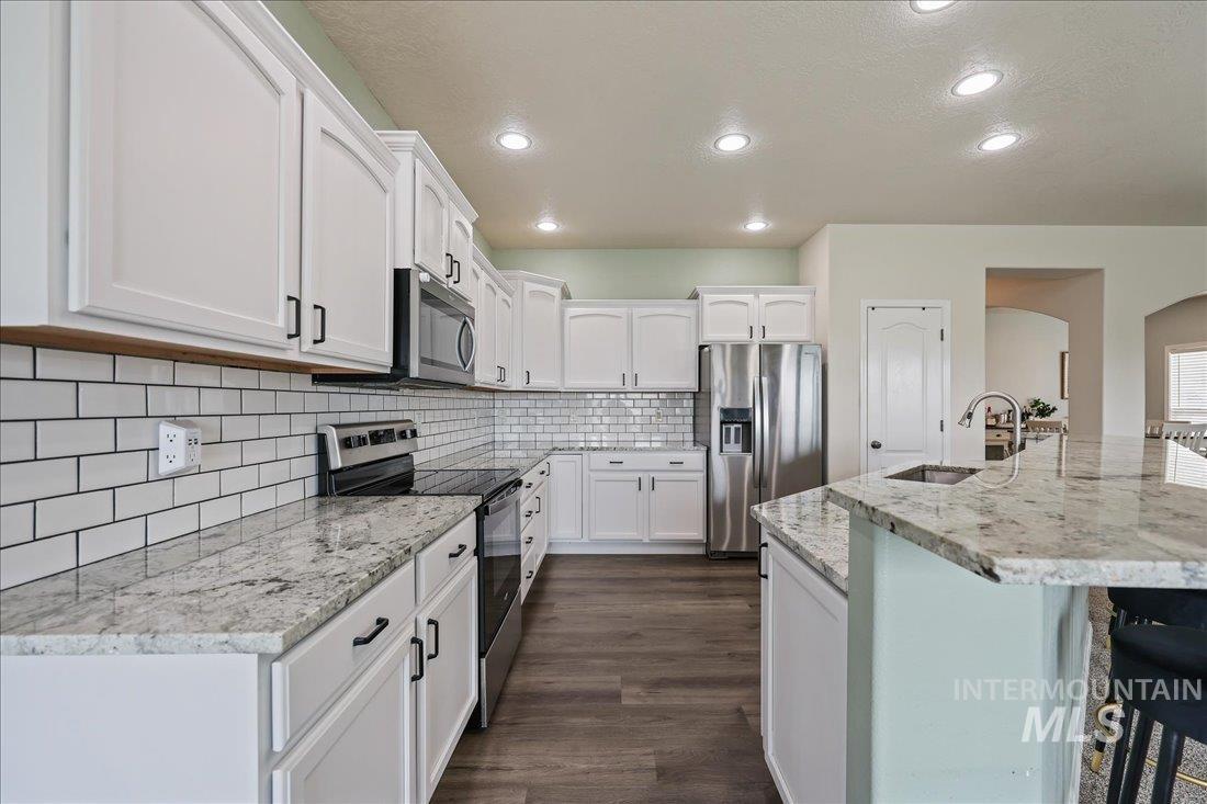 Kitchen with appliances with stainless steel finishes, a kitchen bar, white cabinetry, light stone counters, and arched walkways