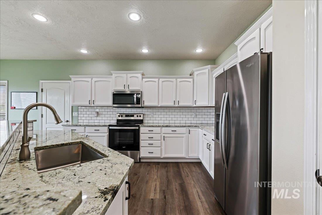 Kitchen with stainless steel appliances, white cabinets, a textured ceiling, light stone countertops, and recessed lighting