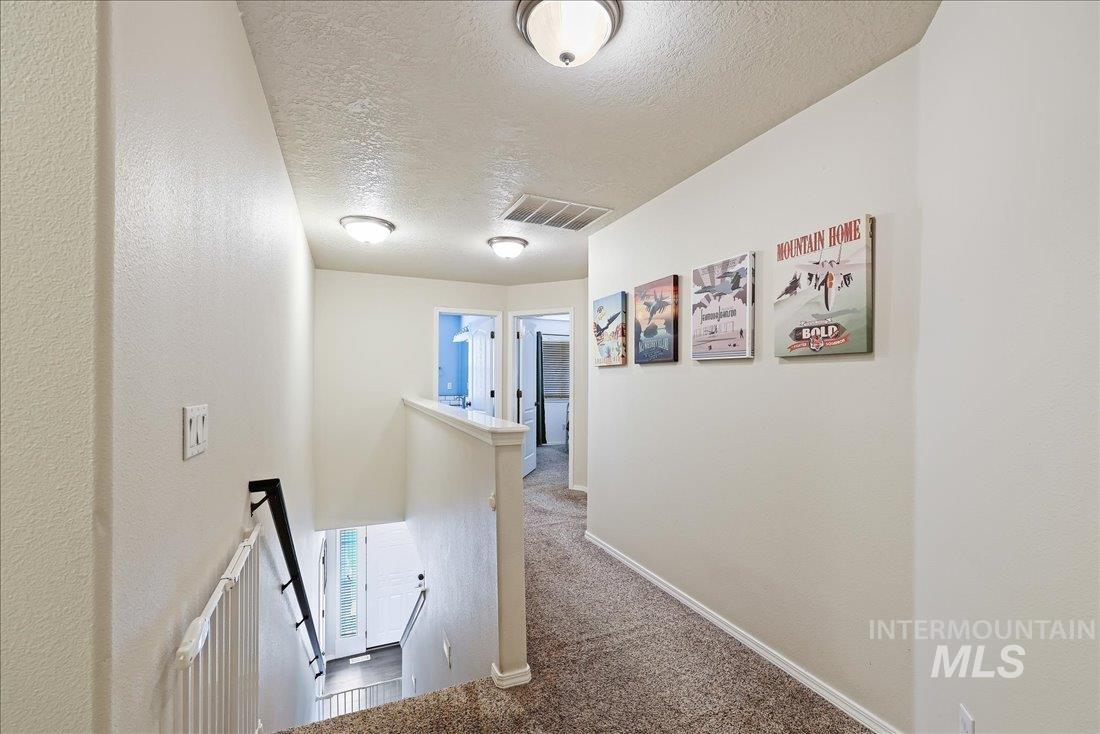 Hallway featuring an upstairs landing, carpet floors, and a textured ceiling
