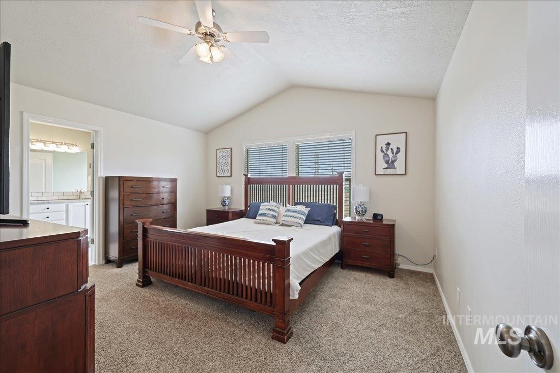 Bedroom with lofted ceiling, light carpet, a ceiling fan, ensuite bathroom, and a textured ceiling