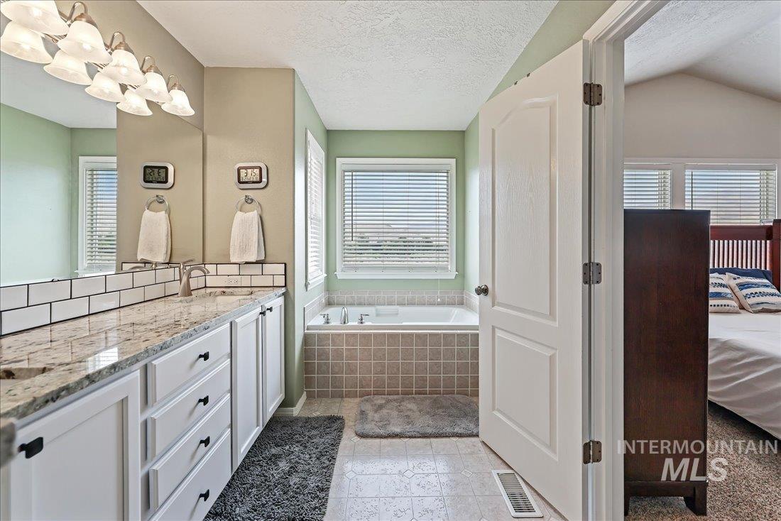 Ensuite bathroom featuring vanity, a garden tub, and a textured ceiling