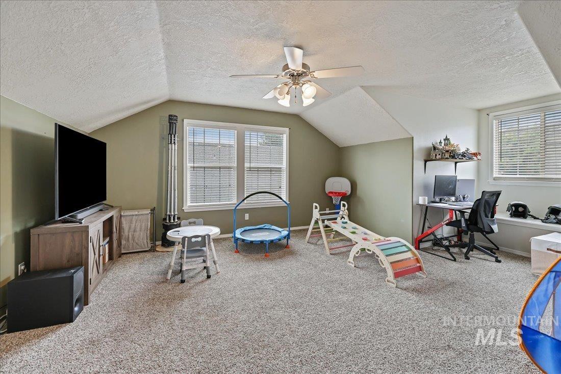 Recreation room featuring carpet floors, a textured ceiling, lofted ceiling, a ceiling fan, and a desk