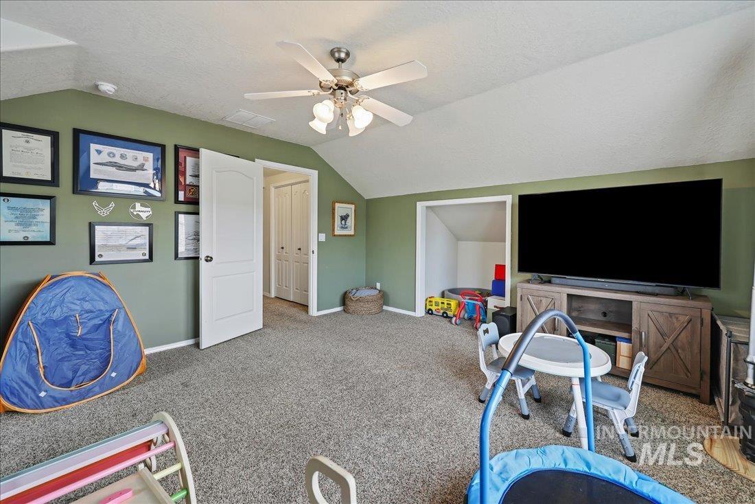 Rec room featuring lofted ceiling, carpet, a textured ceiling, and a ceiling fan