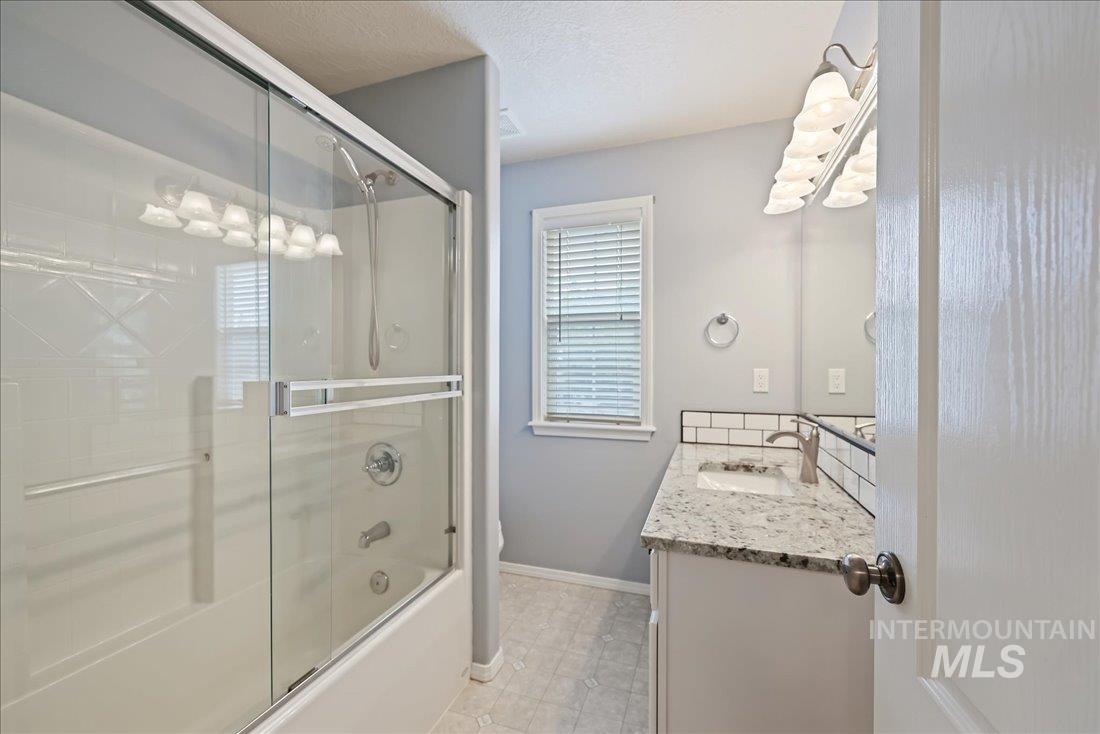 Bathroom with vanity, shower / bath combination with glass door, a textured ceiling, and light tile patterned floors
