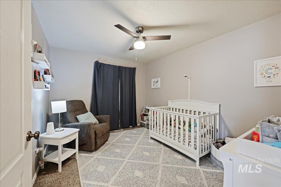 Bedroom featuring a nursery area, a ceiling fan, light colored carpet, and a textured ceiling