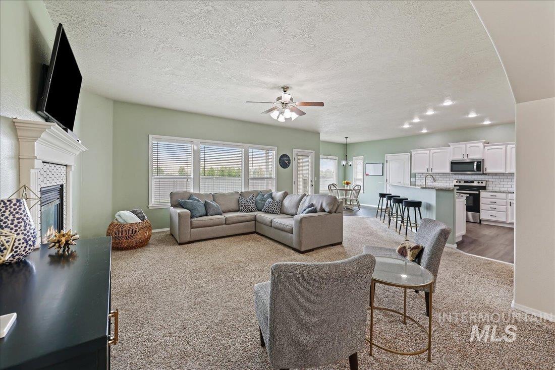 Living room with light colored carpet, a textured ceiling, ceiling fan, and a tiled fireplace