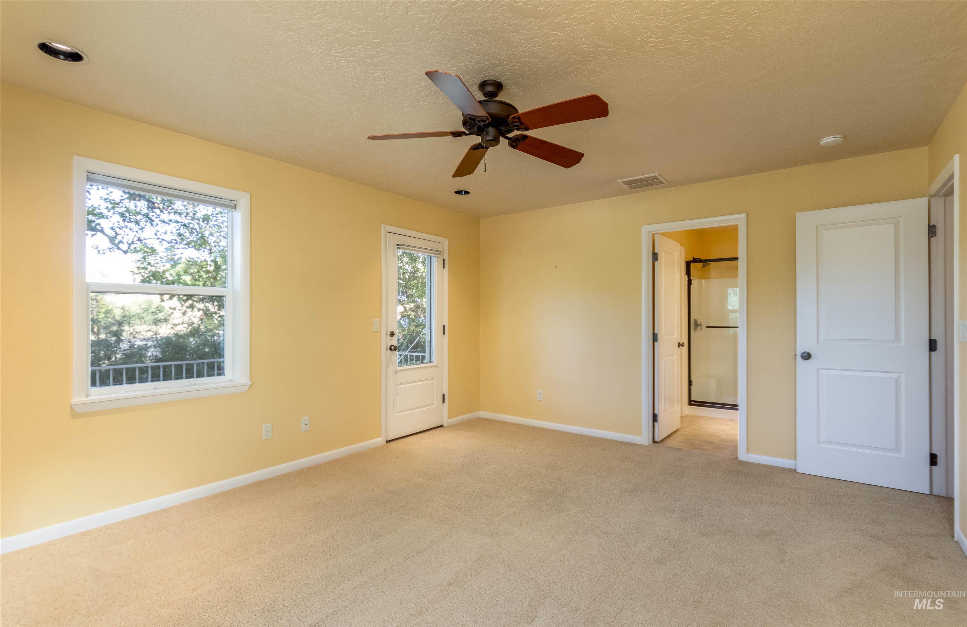 Master bedroom with light carpet, a textured ceiling, a ceiling fan, exterior door to deck and ensuite bathroom