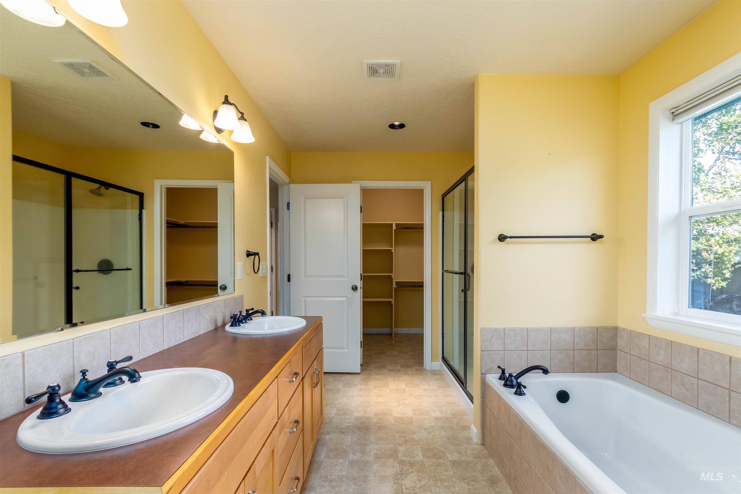 Full bathroom featuring a walk in closet, walk in shower, a bath, and double vanity