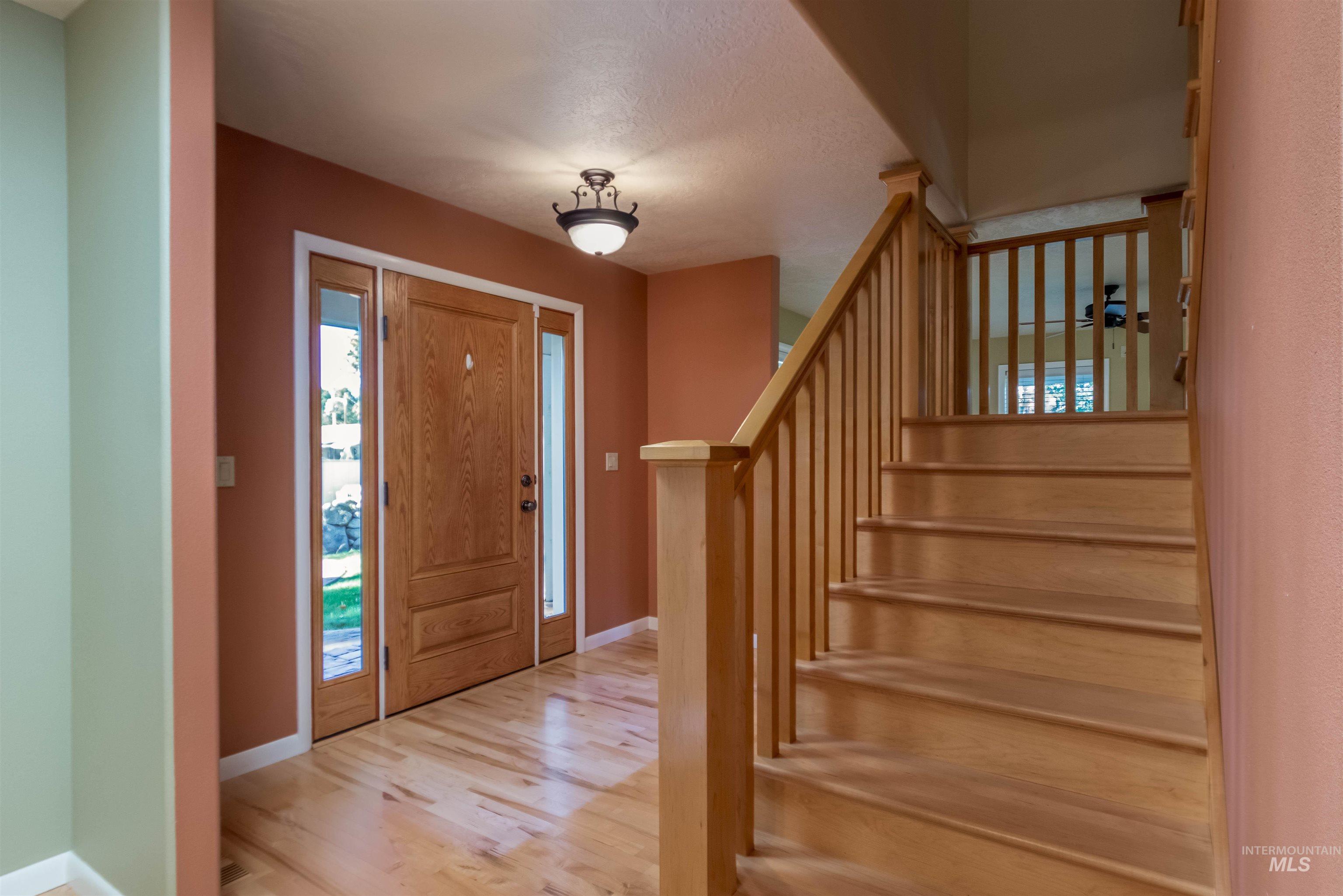 Entryway with light maple flooring, staircase, dining & kitchen to the right of the staircase and living room to the left of the staircase