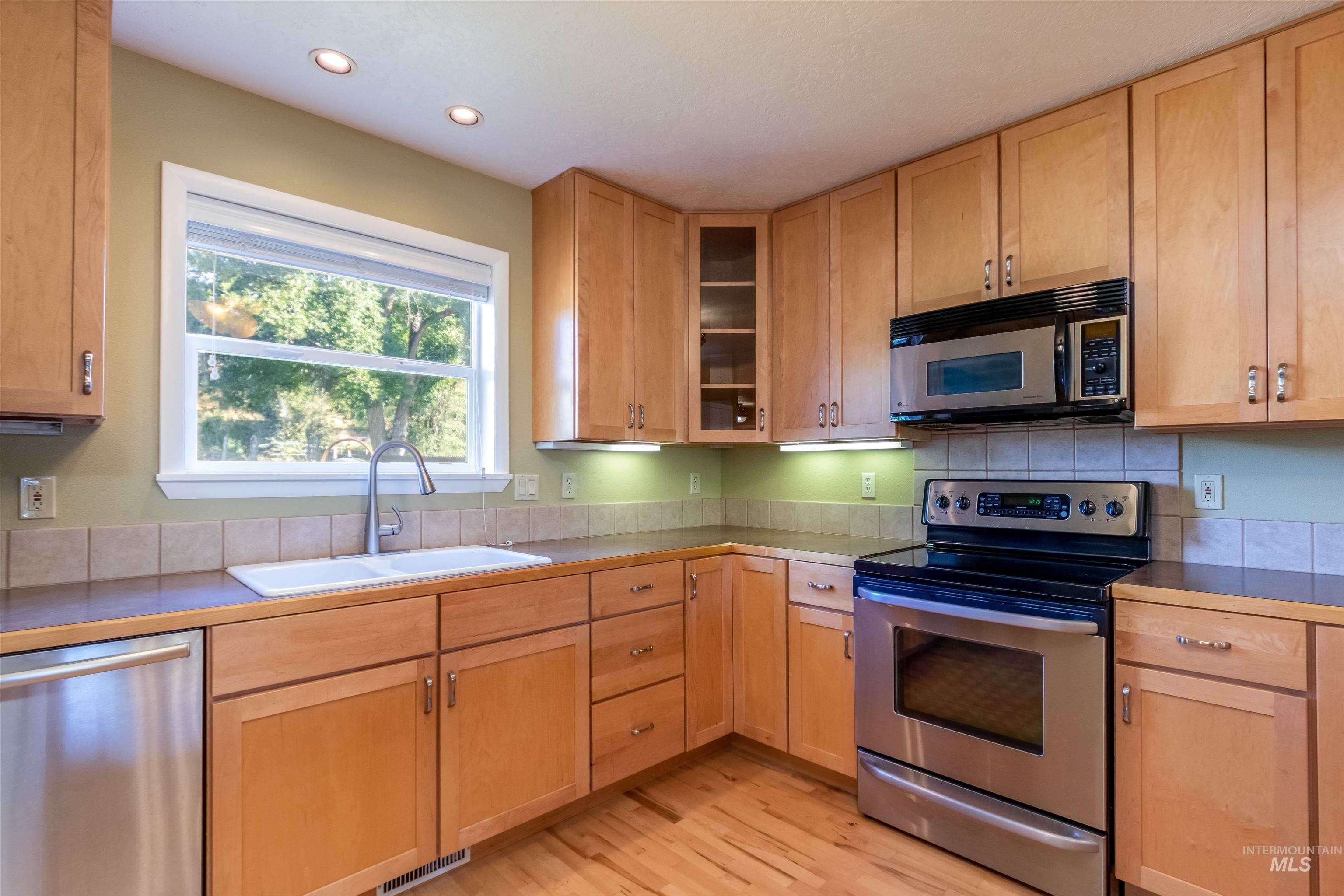 Kitchen with appliances with stainless steel finishes, maple hardwood flooring, recessed lighting, and glass insert cabinets