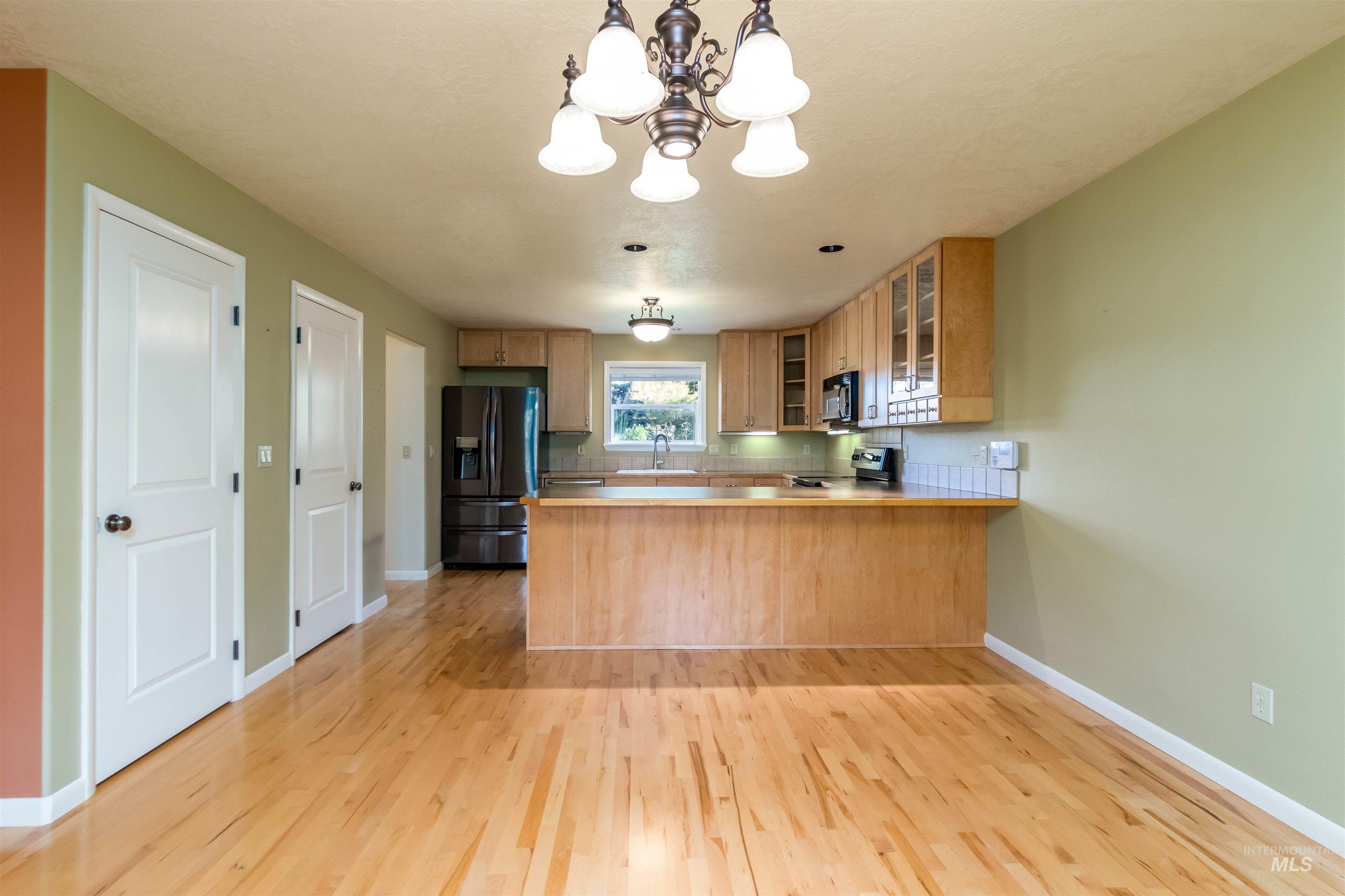 Kitchen featuring glass insert cabinets, stainless steel fridge, a chandelier, and electric range oven
