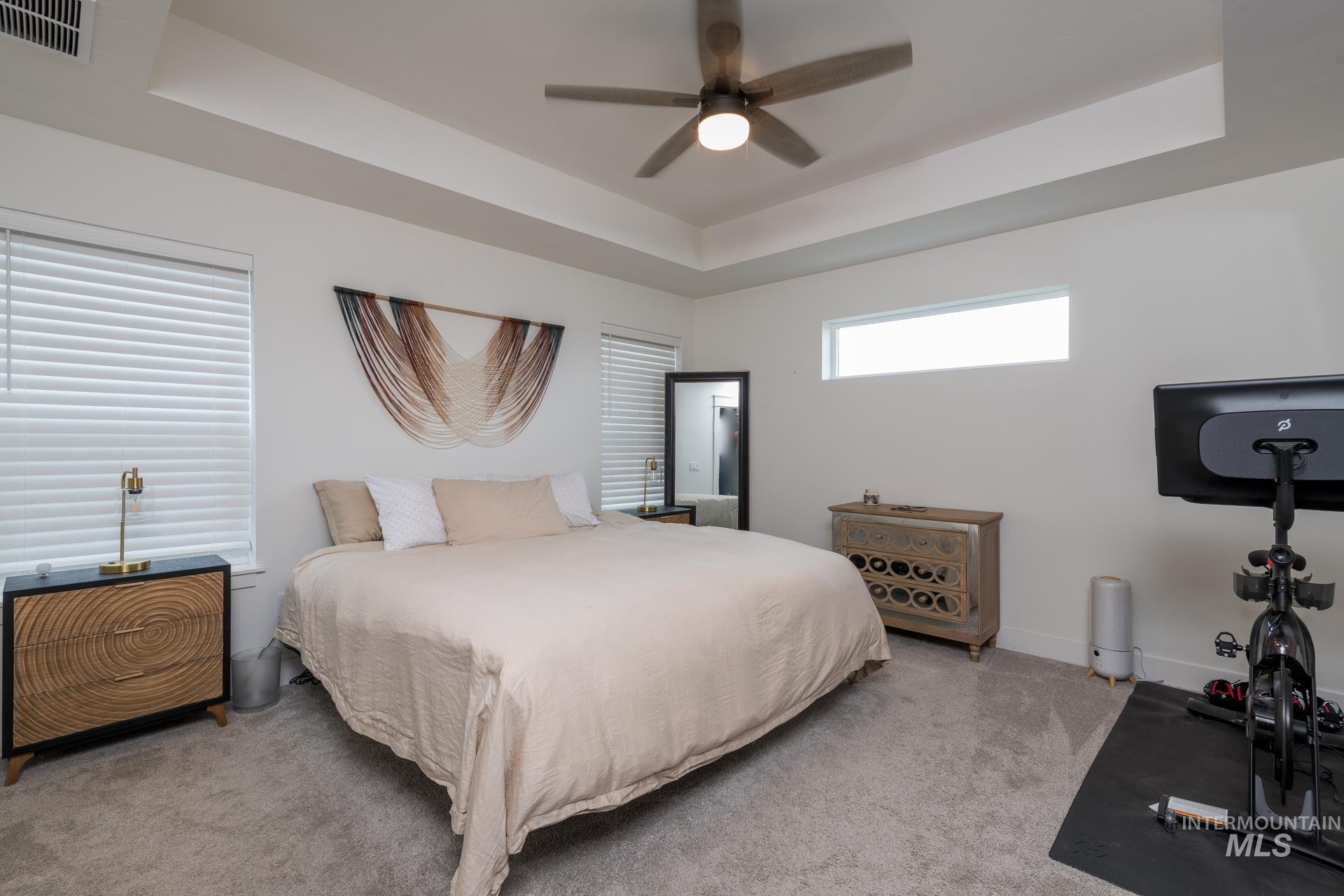 Carpeted bedroom featuring a raised ceiling and ceiling fan
