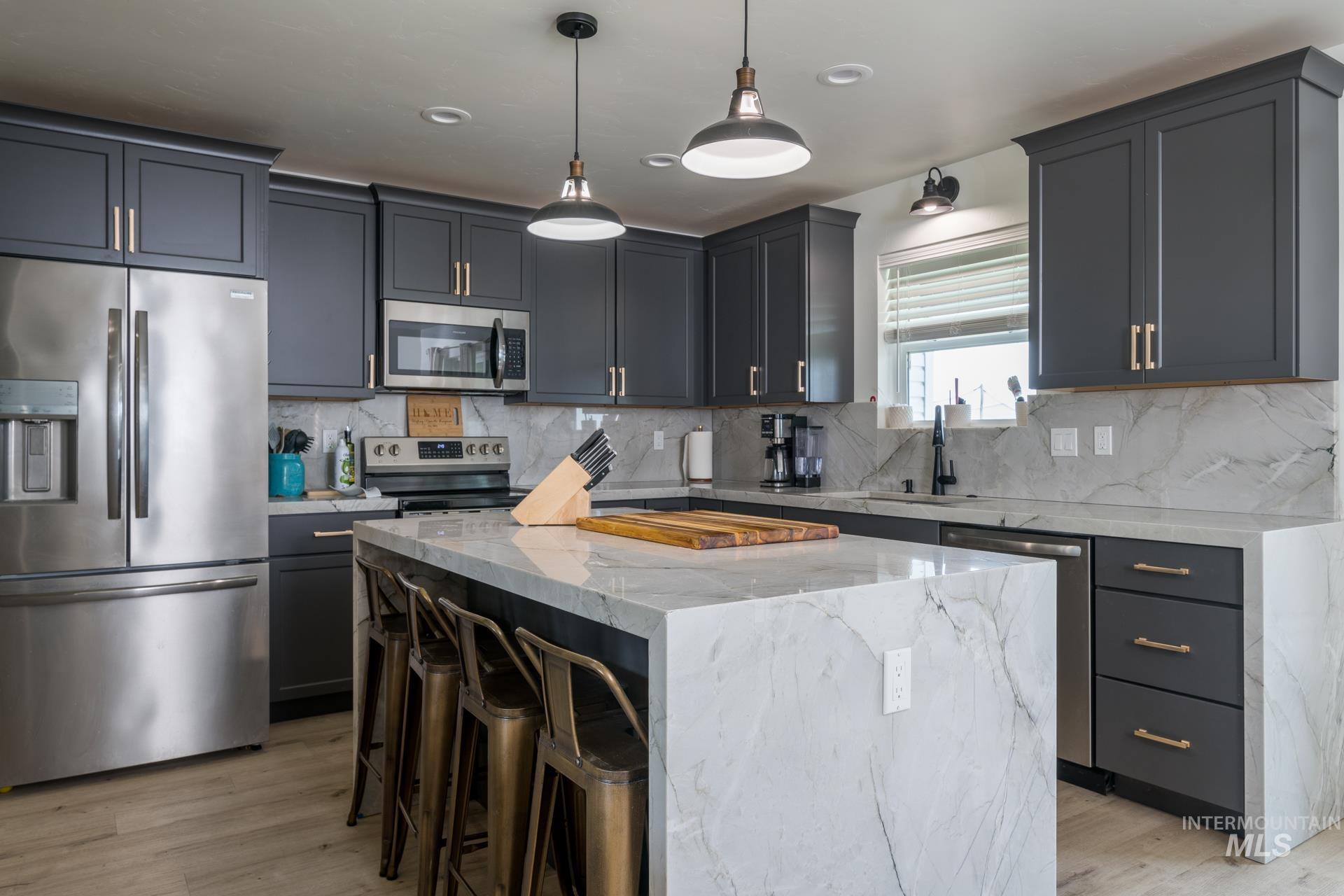 Kitchen with stainless steel appliances, light stone countertops, a center island, hanging light fixtures, and a kitchen bar