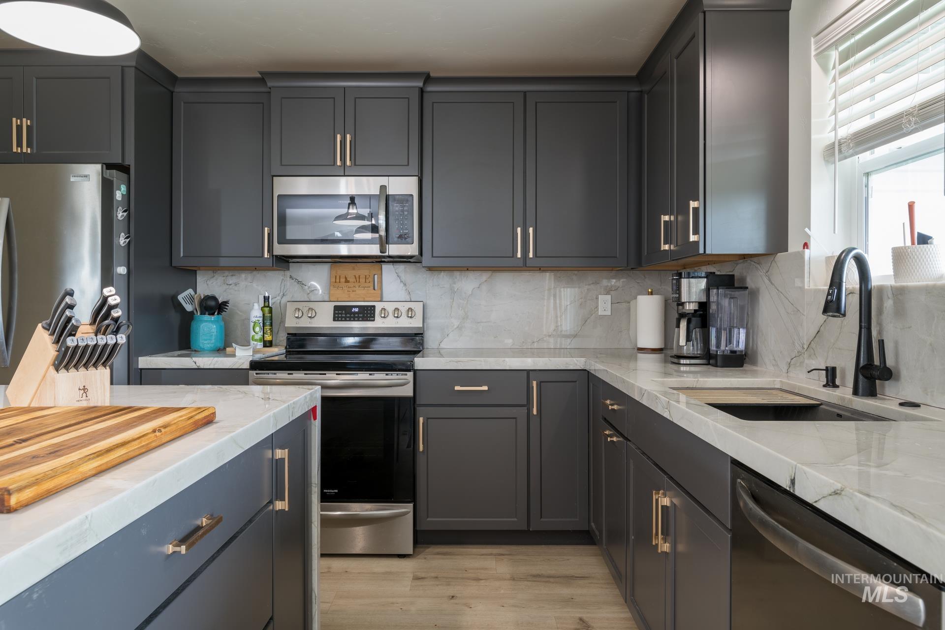 Kitchen featuring stainless steel appliances, tasteful backsplash, light wood finished floors, light stone countertops, and gray cabinetry