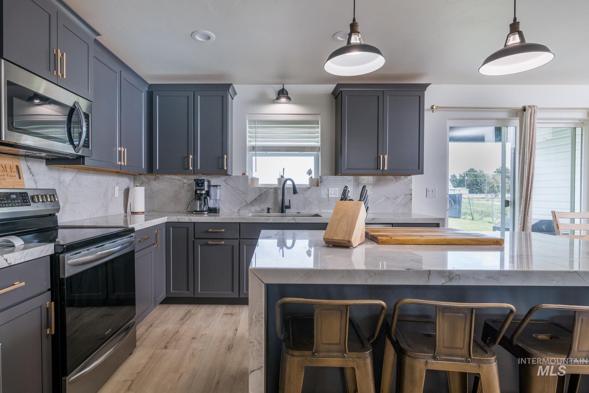 Kitchen featuring appliances with stainless steel finishes, light stone counters, a kitchen bar, pendant lighting, and light wood-type flooring