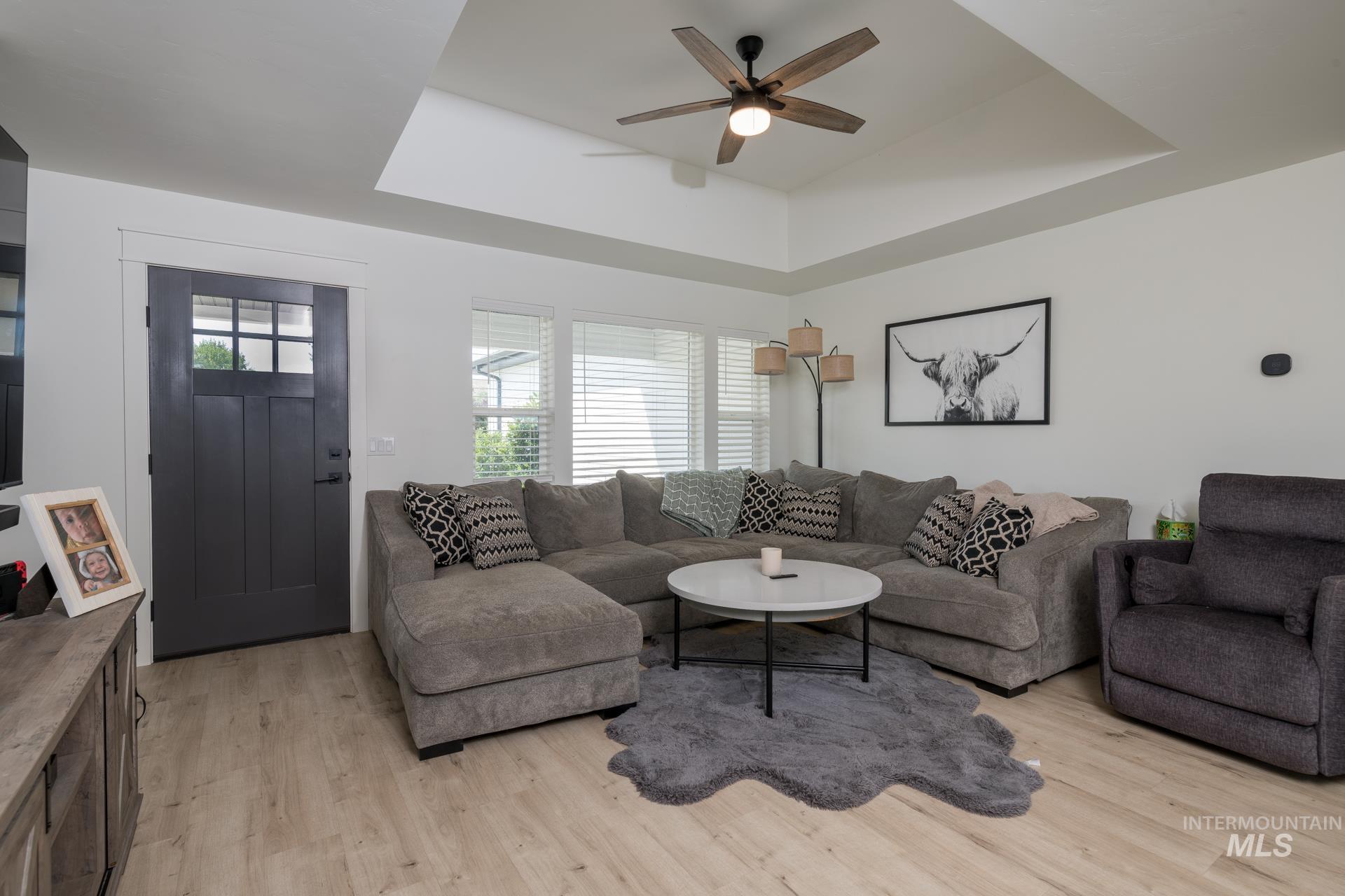Living room with a raised ceiling, light wood finished floors, and a ceiling fan