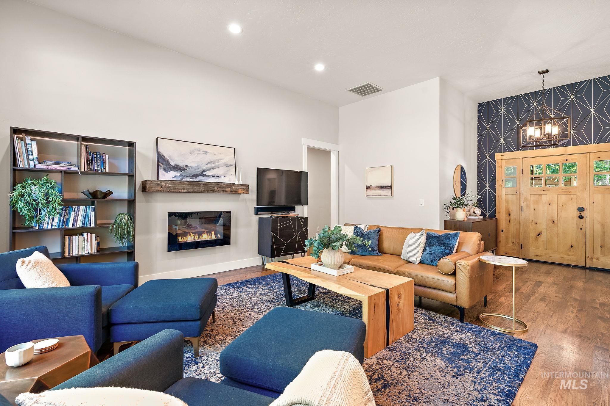 Living room featuring wood finished floors, a chandelier, a glass covered fireplace, recessed lighting, and an accent wall