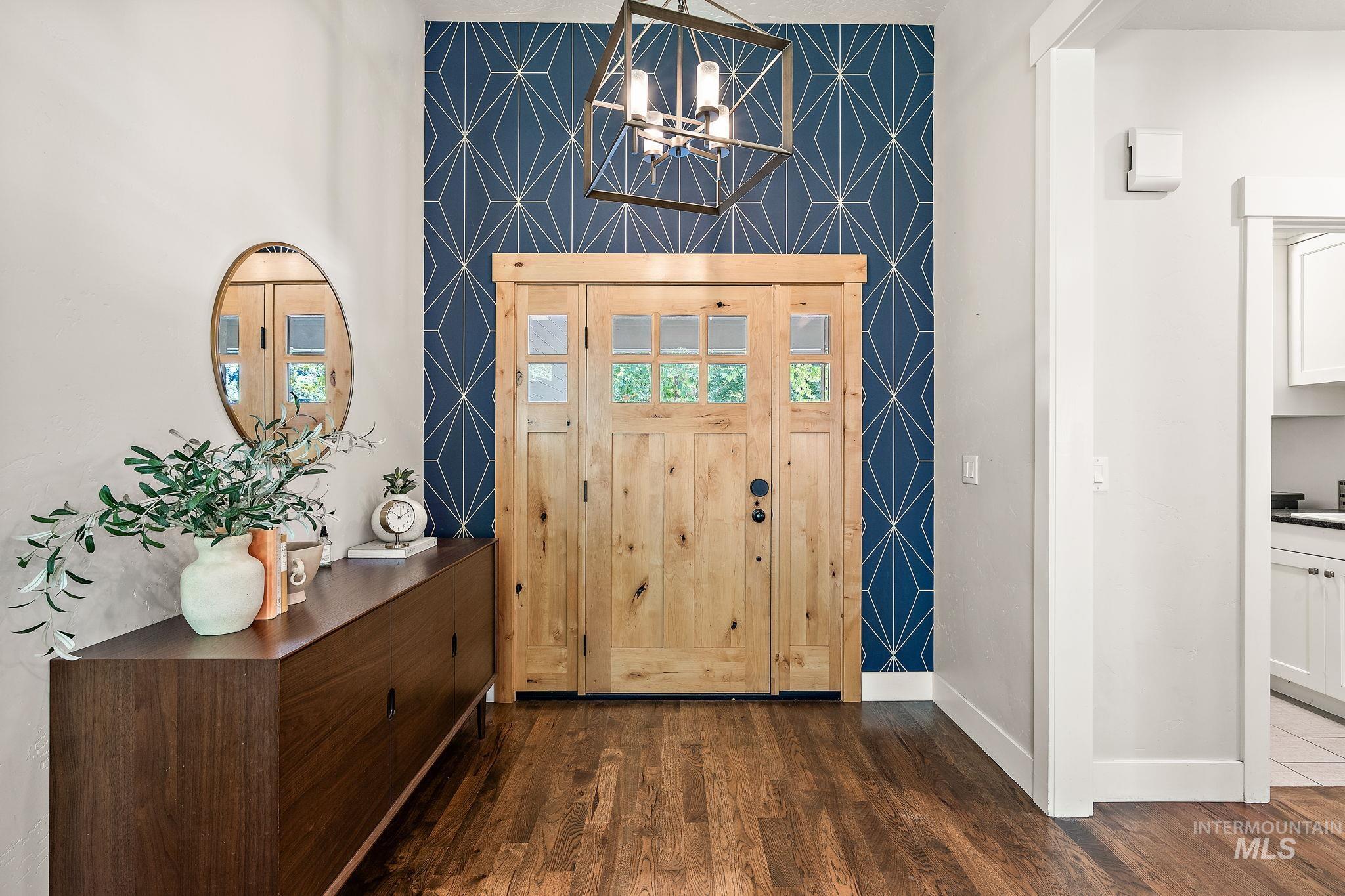 Foyer entrance featuring dark wood-style flooring, a chandelier, and an accent wall