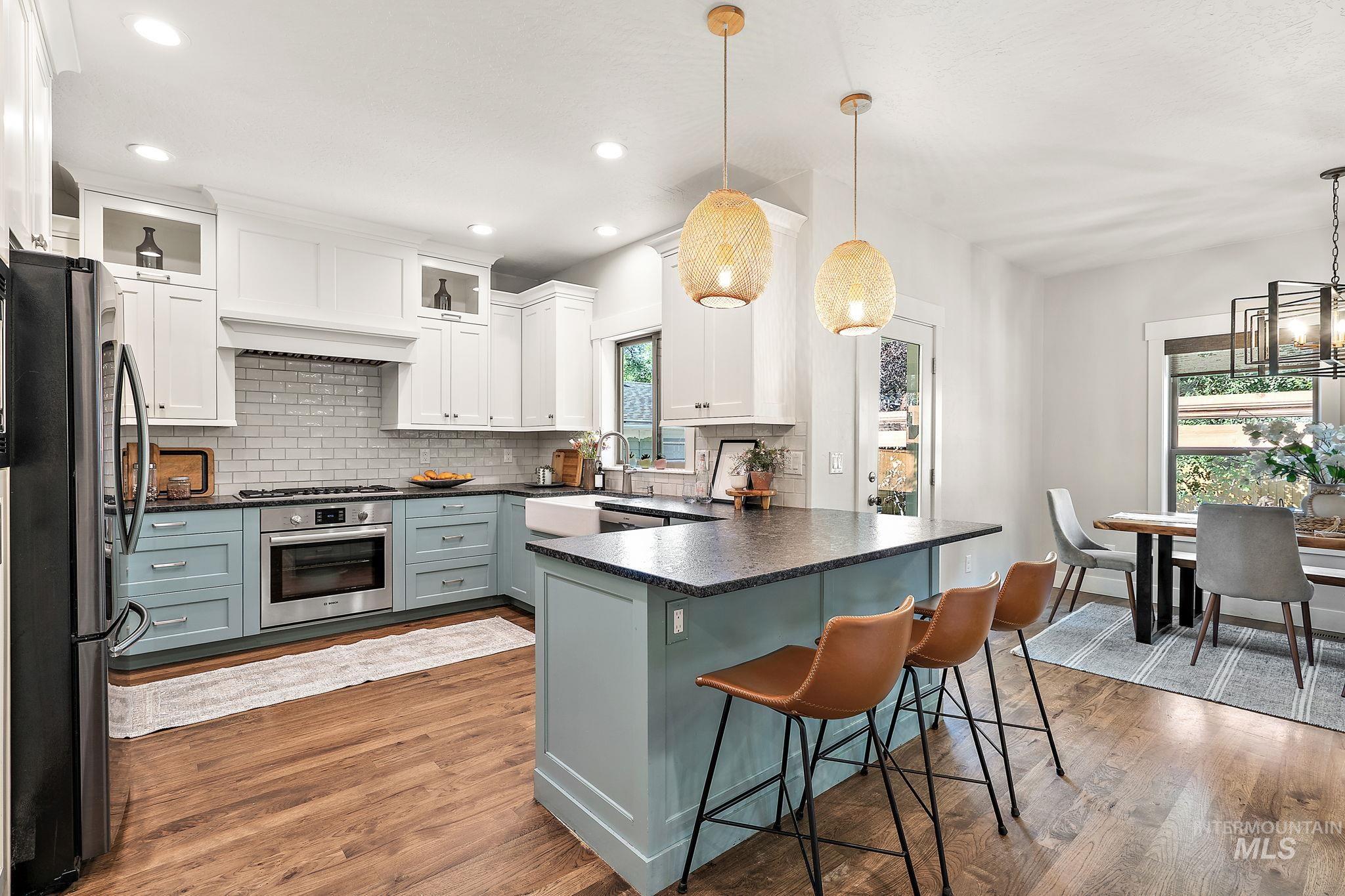 Kitchen with backsplash, stainless steel appliances, light wood-style floors, white cabinetry, and hanging light fixtures