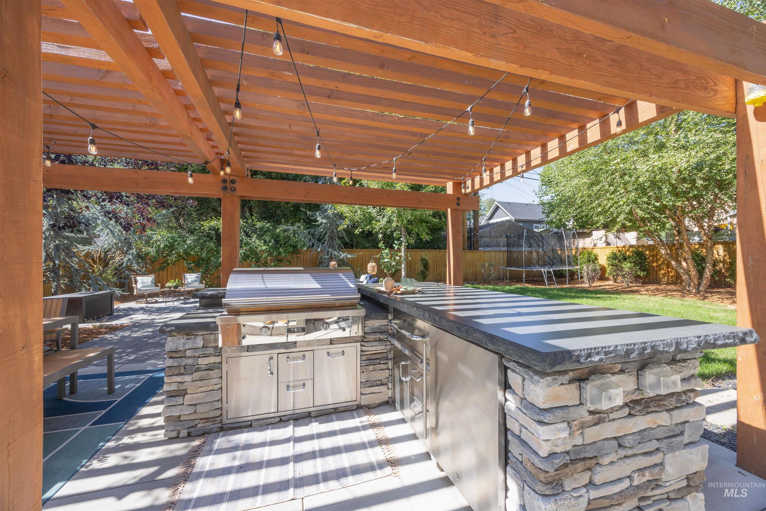 Fenced backyard with a trampoline, a patio area, and exterior kitchen