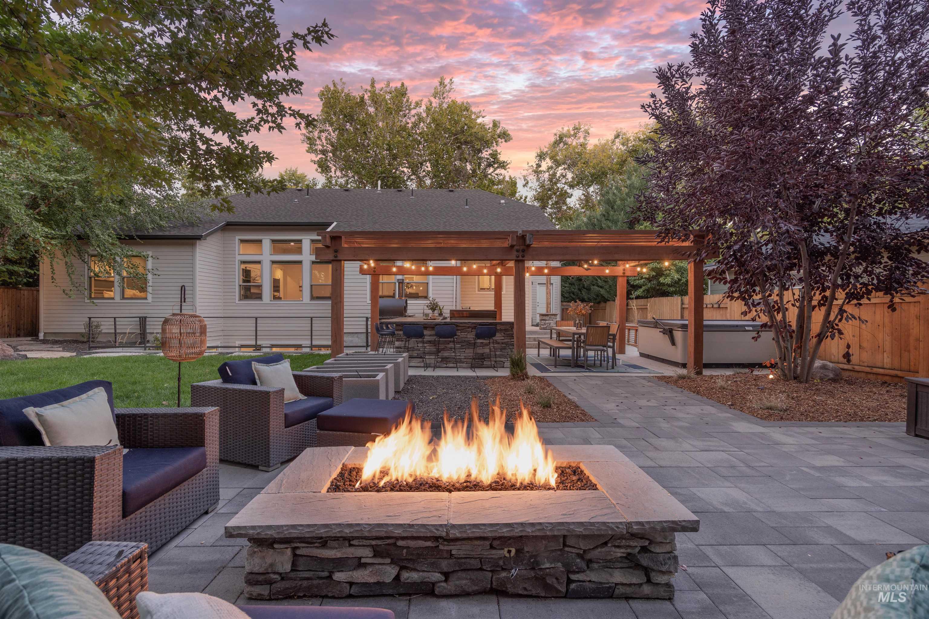 Patio terrace at dusk with a hot tub, a patio, a pergola, a fenced backyard, and an outdoor living space with a fire pit