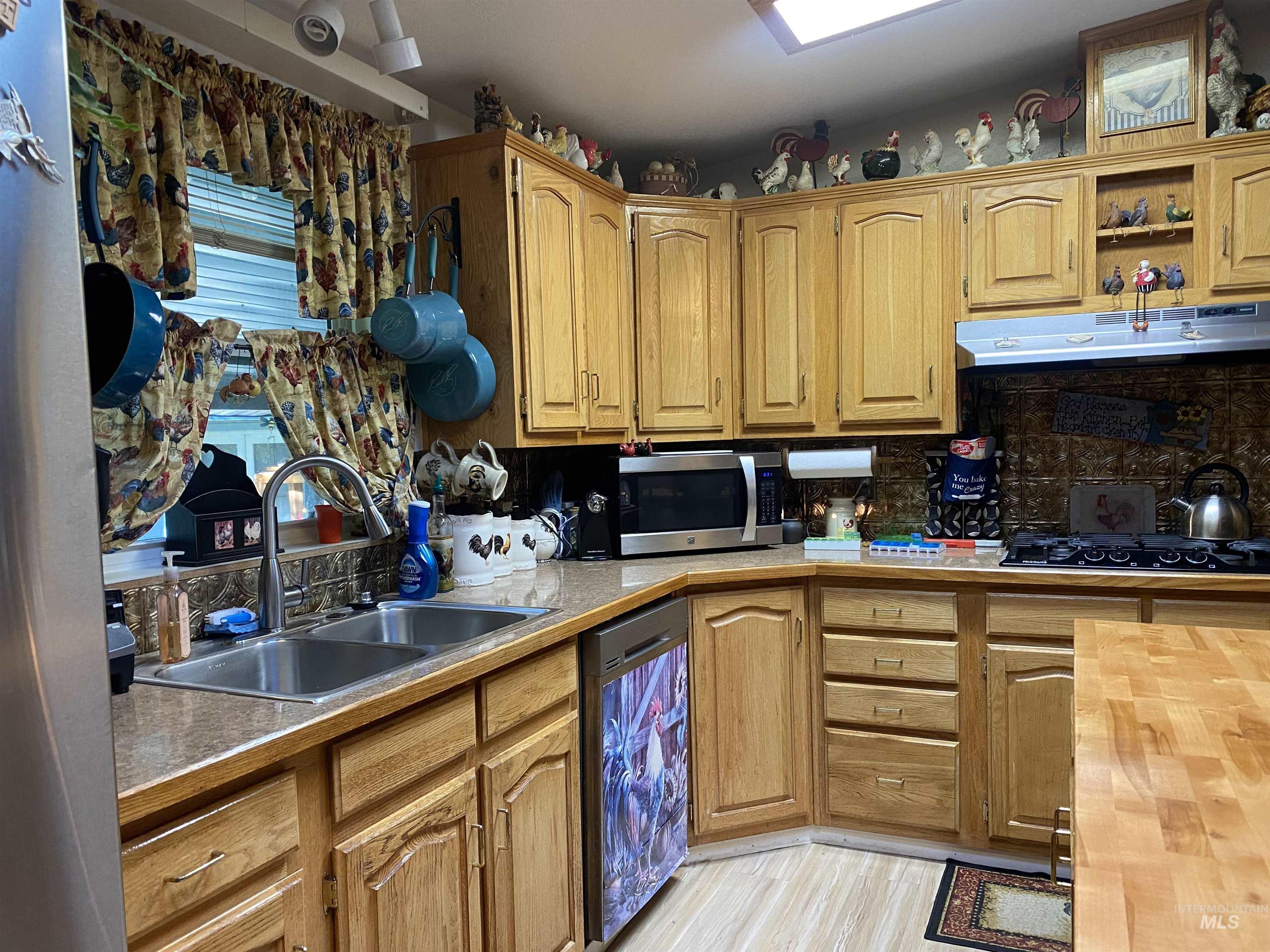 Kitchen featuring light countertops, open shelves, appliances with stainless steel finishes, and under cabinet range hood